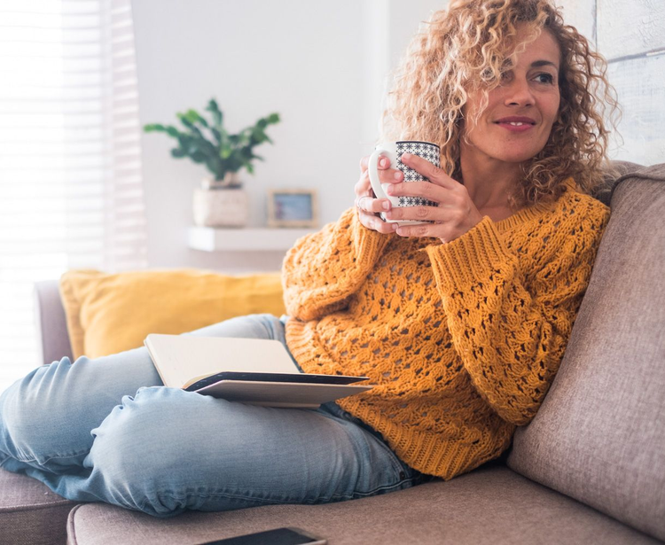 Woman relaxing on a couch with a mug and open book in a bright living room