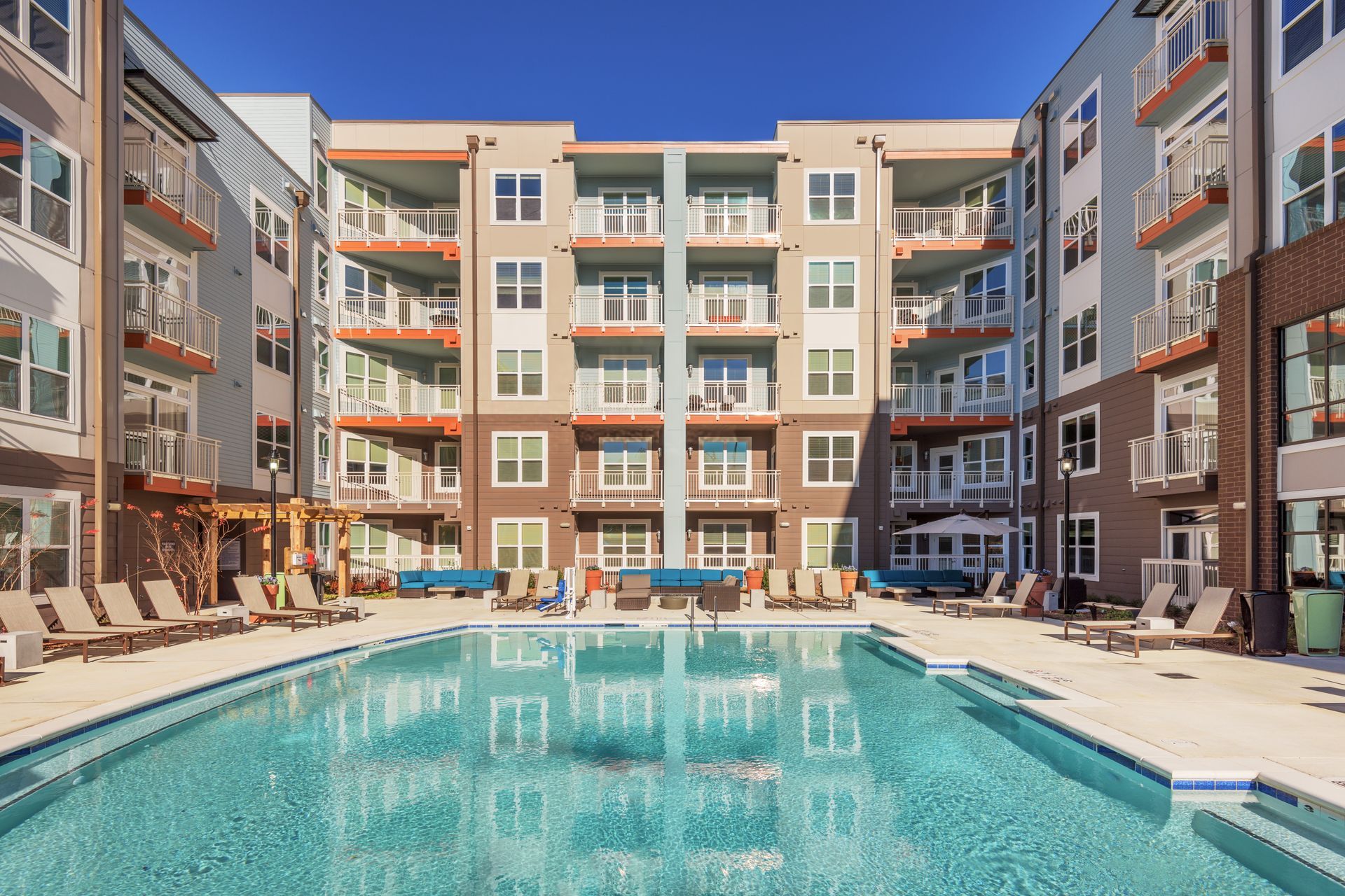 Apartment building with pool. Exterior view with balconies, sun loungers, and blue water. Sunny day.