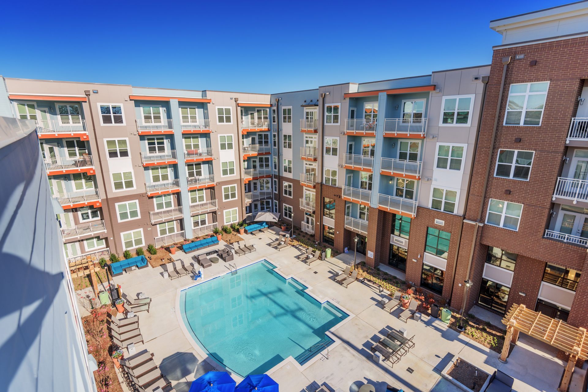 Courtyard with pool surrounded by modern apartment building, blue sky.