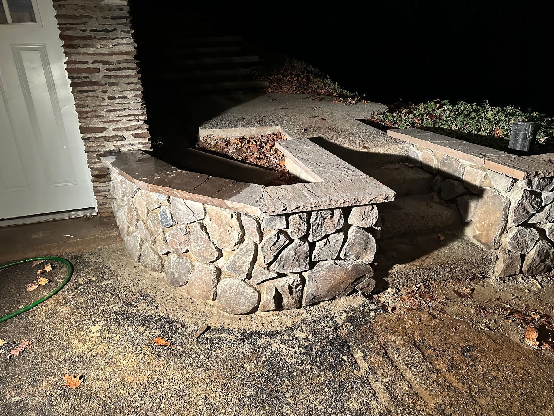 Stone retaining wall with built-in bench and steps beside a house at night
