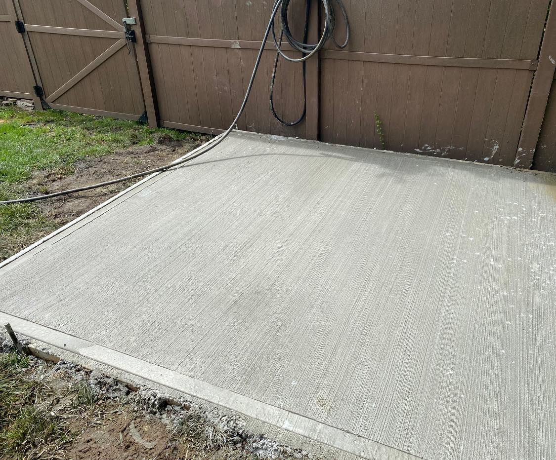 Freshly poured concrete slab beside a wooden fence and gate in a backyard