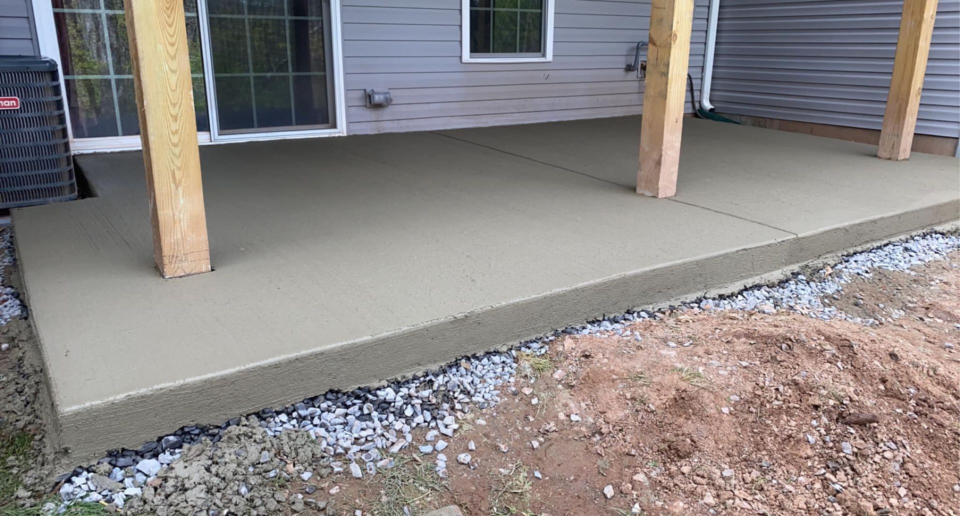 Fresh concrete porch slab with wooden support posts beside a house and dirt ground