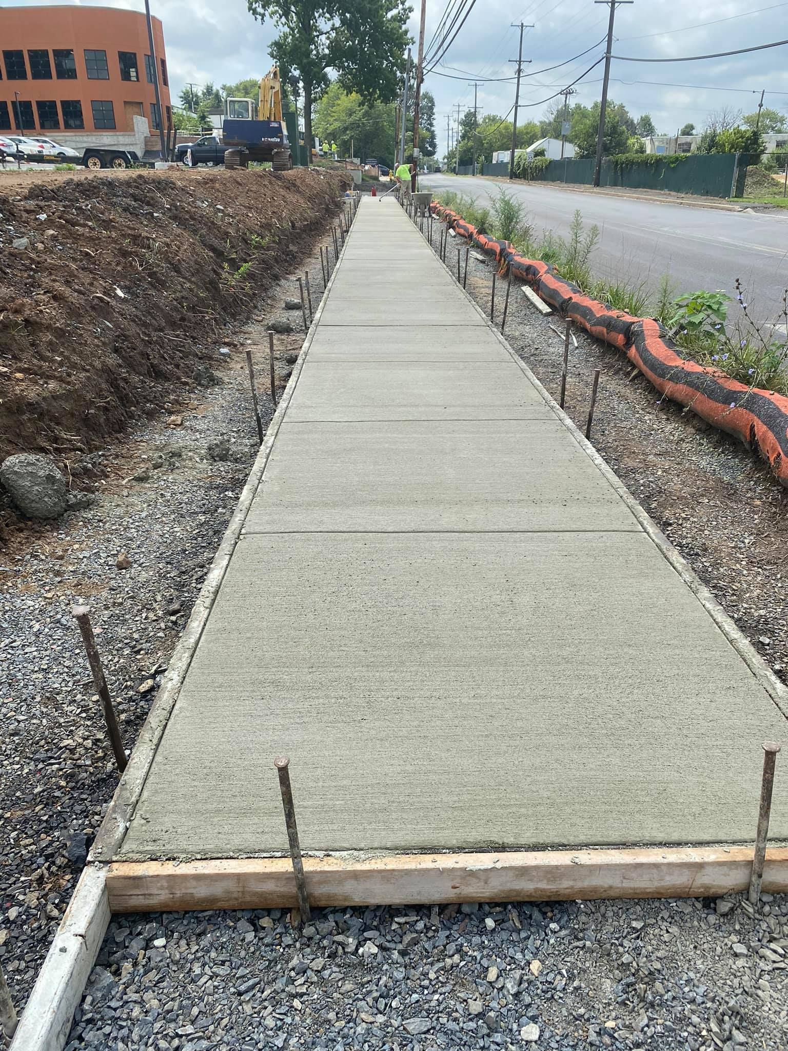 New concrete sidewalk under construction beside a road, with gravel and dirt on both sides.