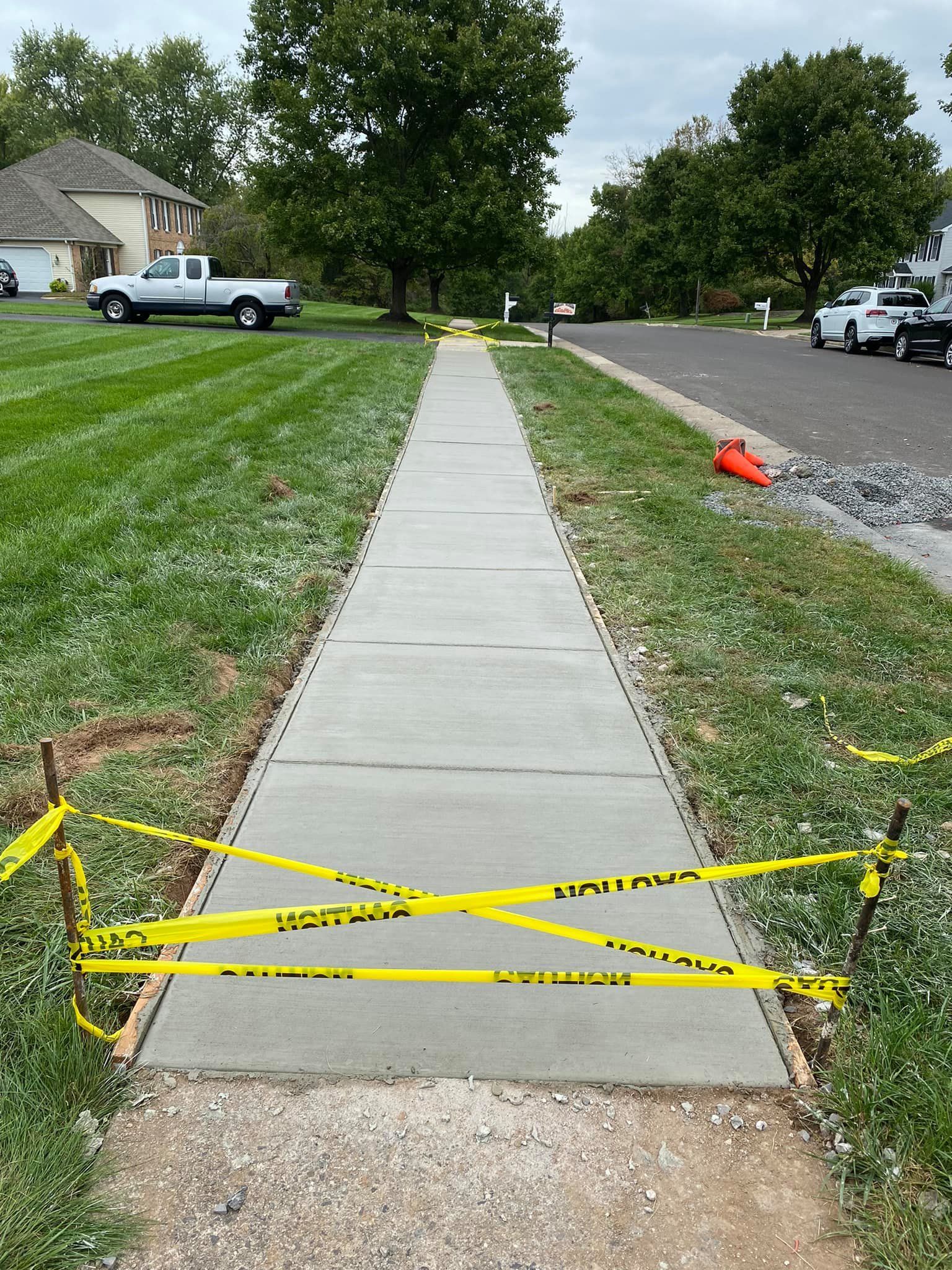 Concrete sidewalk blocked by yellow caution tape between grass lawns in a suburban neighborhood