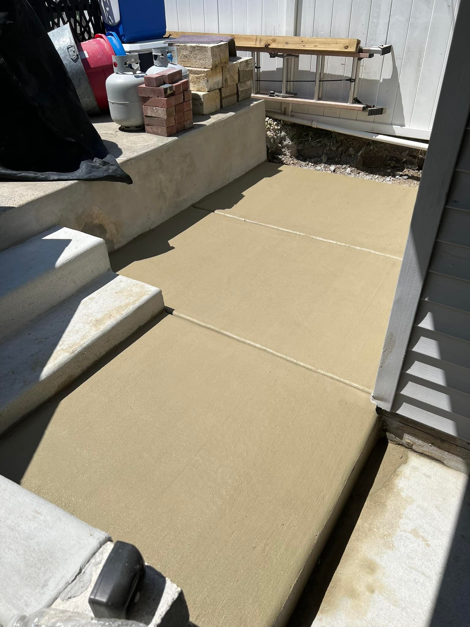 Outdoor patio with tan flooring panels, concrete walls, and a bench against a white fence