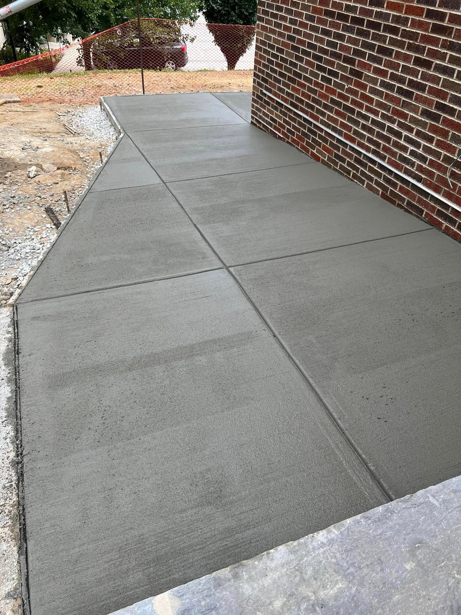 Concrete sidewalk beside a brick building, with a landscaped area and rocks on the left.
