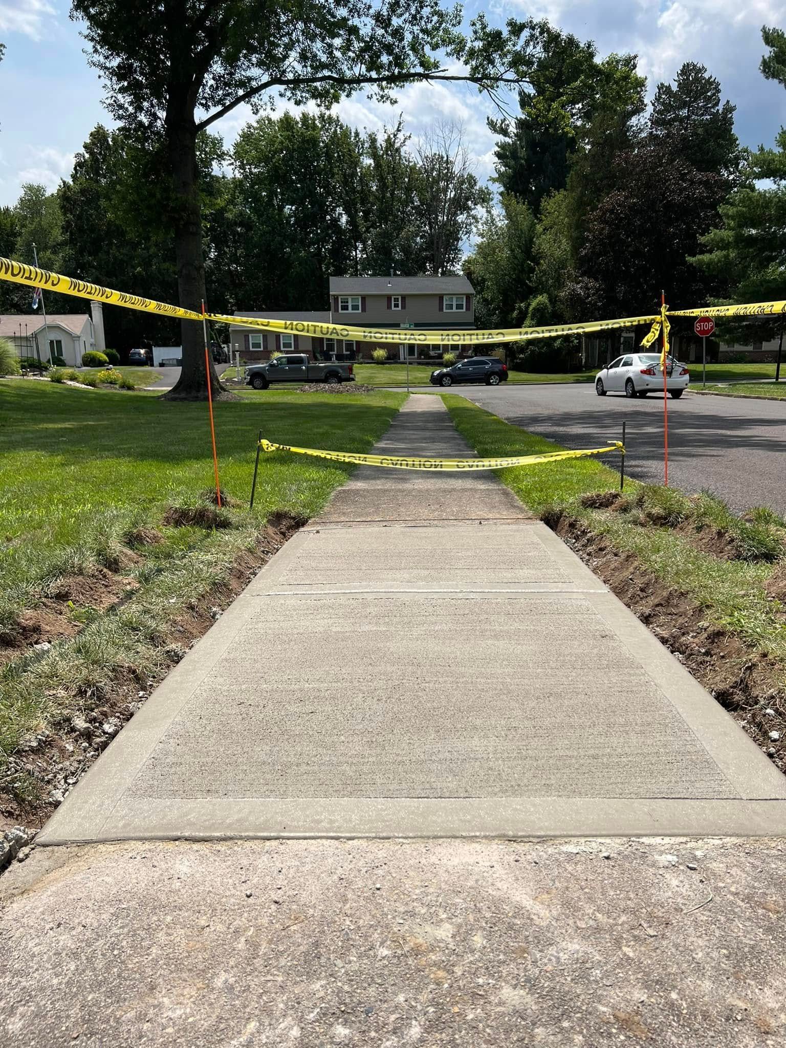 Concrete walkway leading to a house, cordoned off with yellow caution tape in a sunny yard