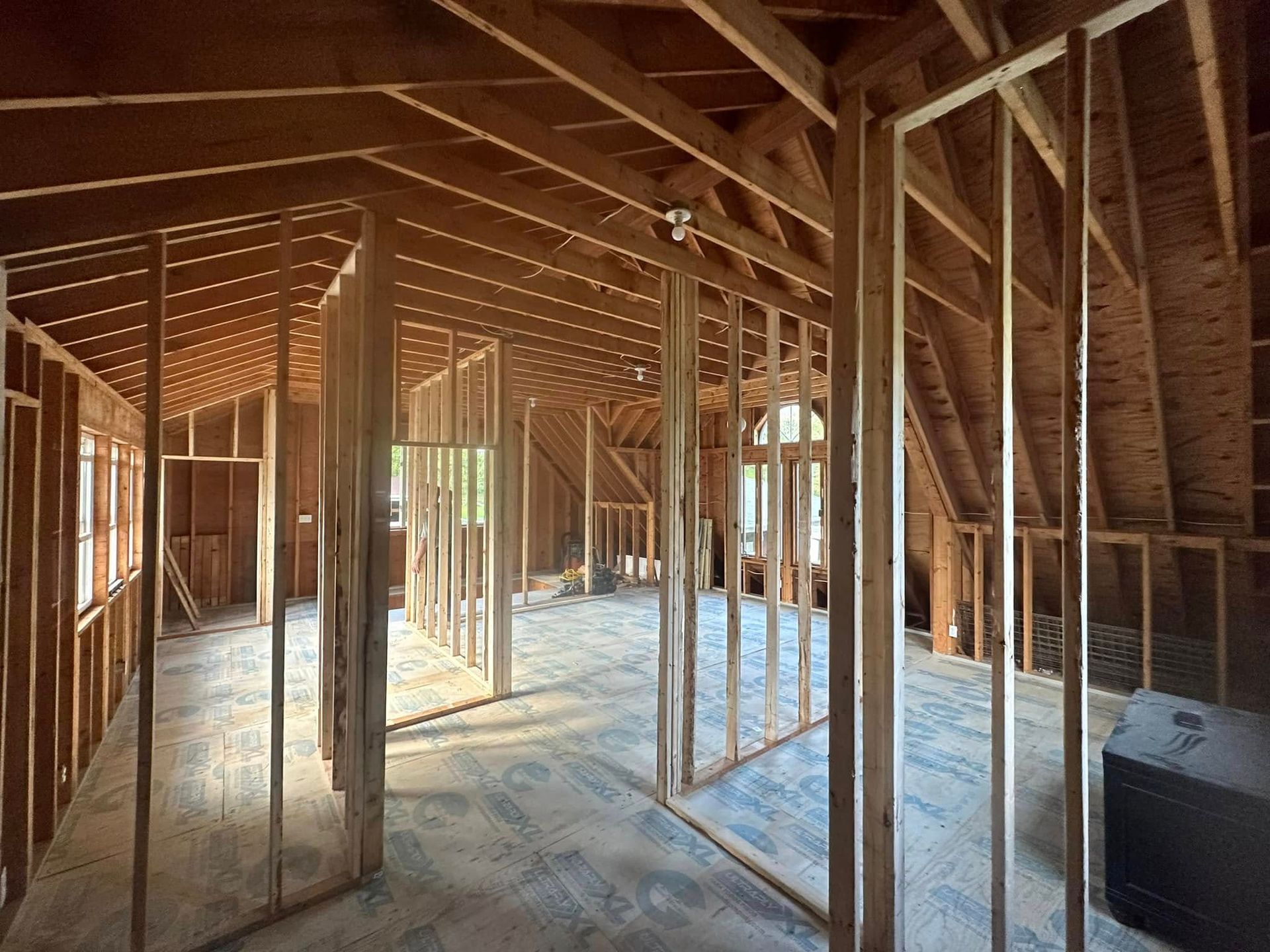 Unfinished attic framed with wooden studs, exposed rafters, and sunlight filtering through the open space.