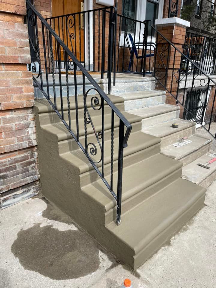 Freshly painted concrete steps with black metal railings leading up to a brick townhouse entrance