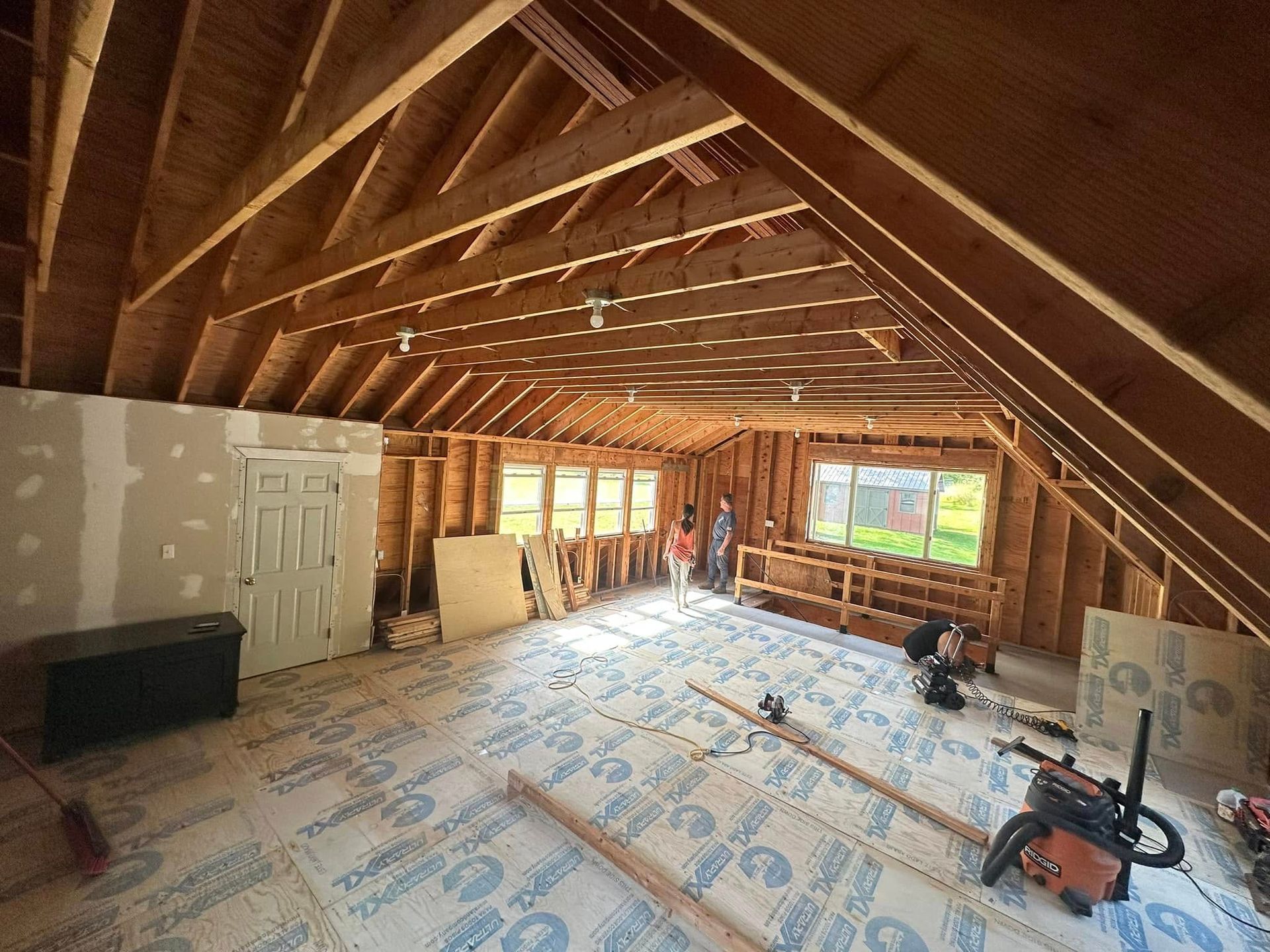 Unfinished attic room with exposed wooden rafters, insulation boards, and construction tools on the floor.