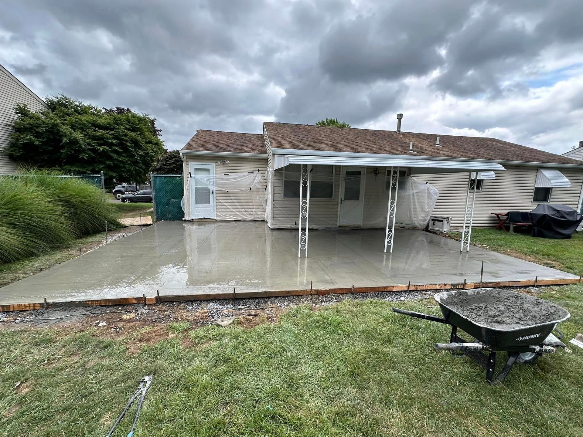 Rain-soaked backyard patio with a white carport, garage, wheelbarrow, and cloudy sky
