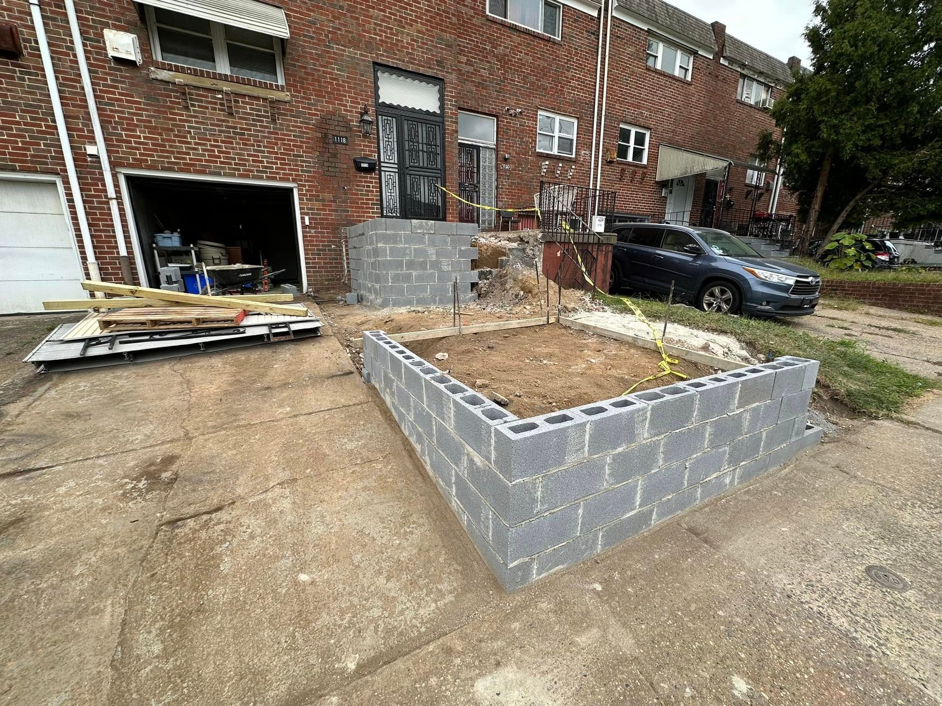 Front yard concrete planter under construction beside a brick townhouse, with a car parked nearby.