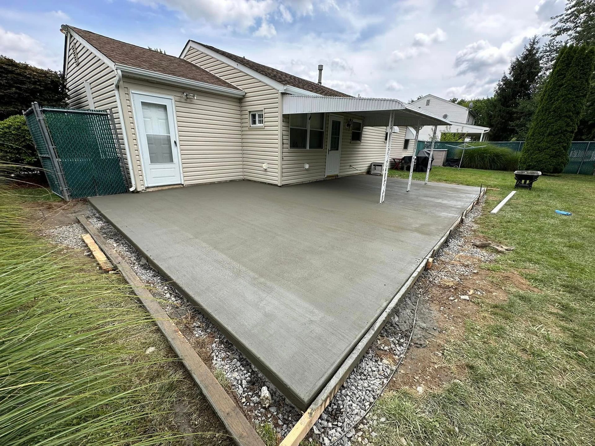 Concrete patio beside a beige house with a covered porch and wet ground after rain