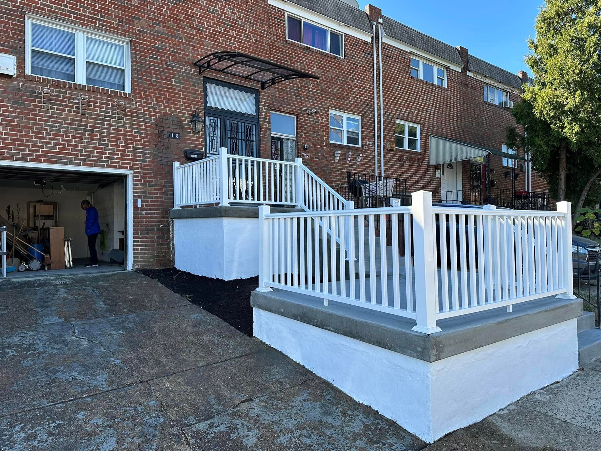 Brick apartment building with white-railed ramps and stairs, and a person standing in an open garage.