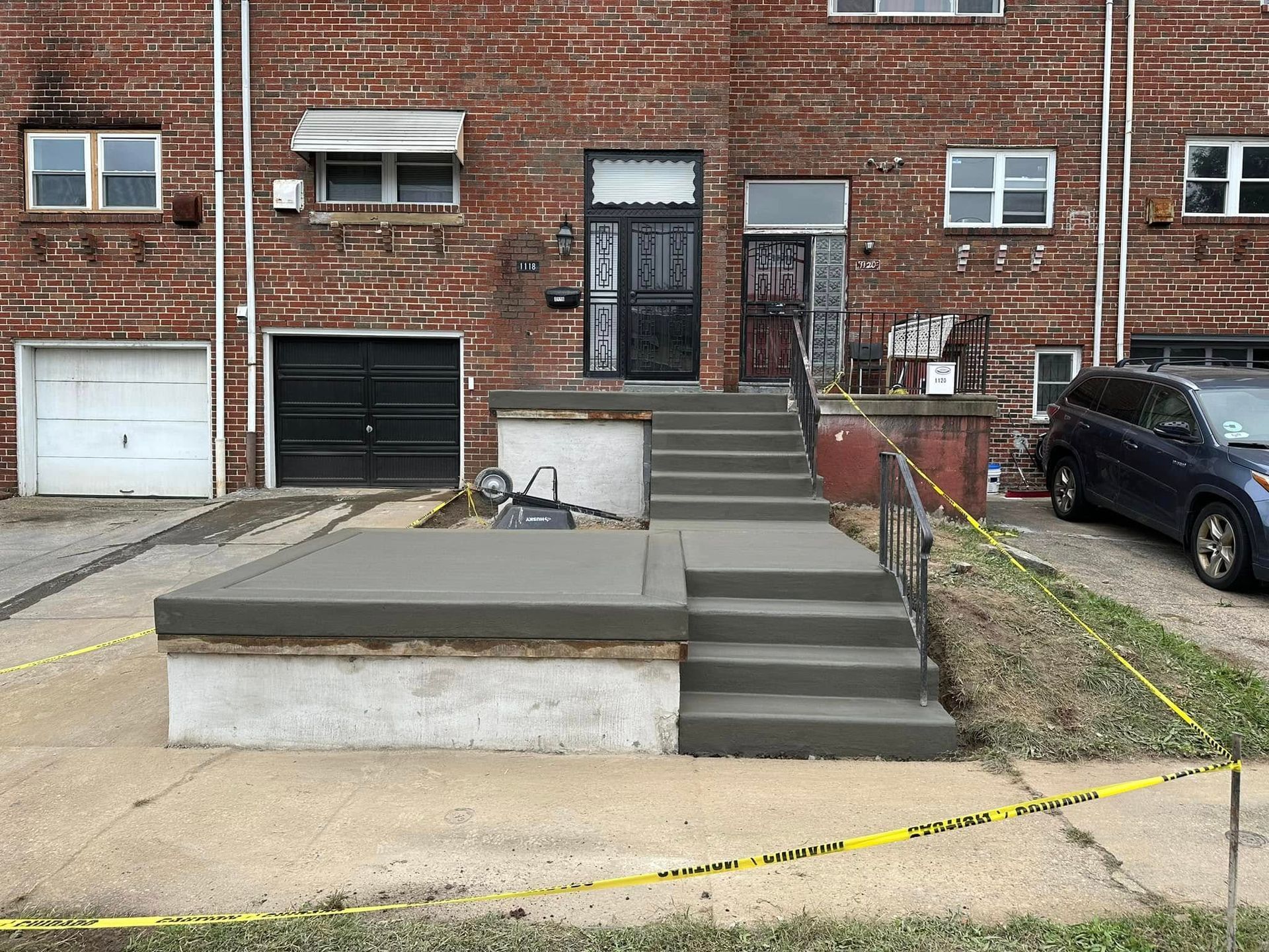 Brick apartment building with front steps, metal railings, garage doors, and caution tape across the sidewalk