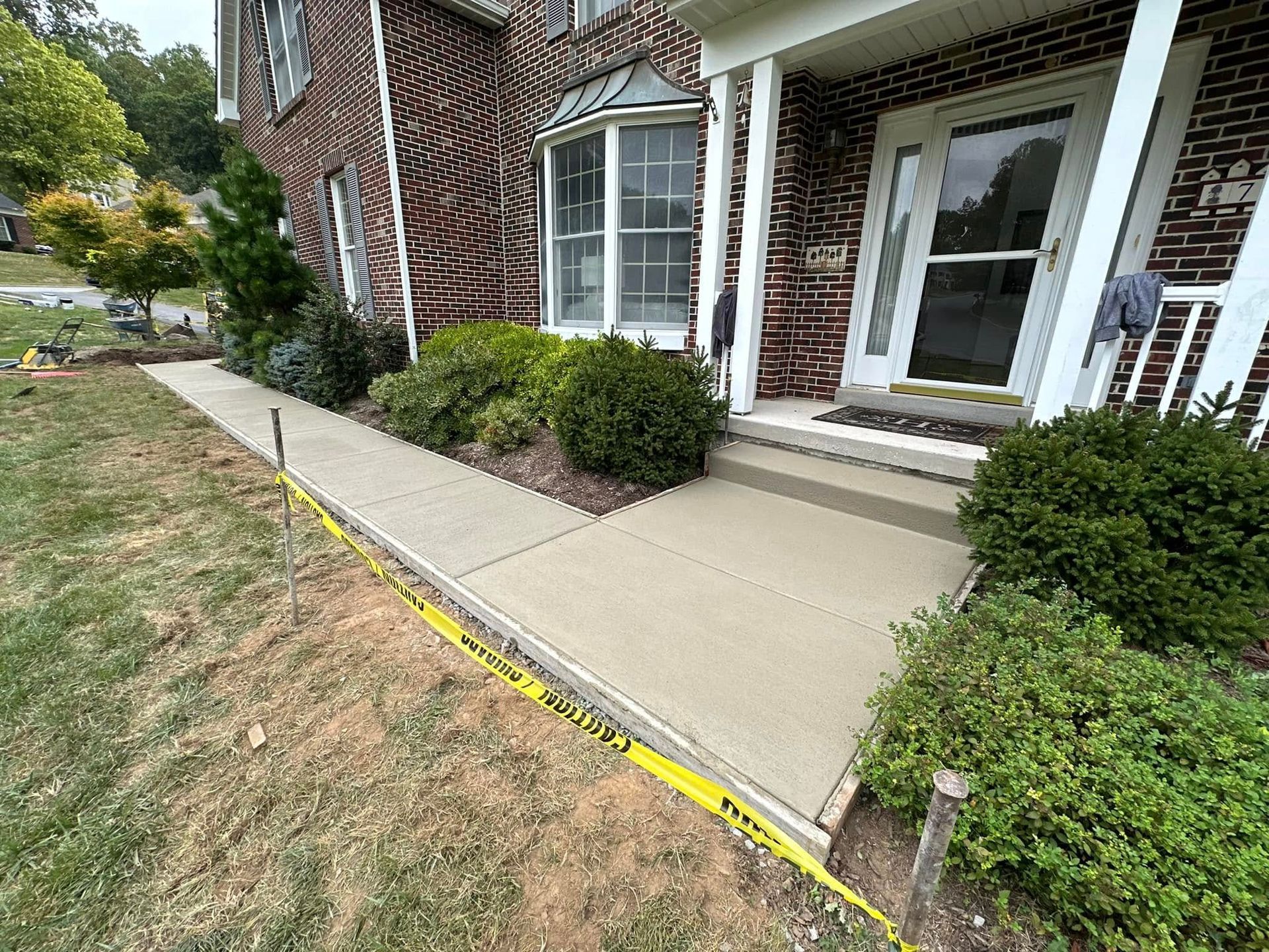 Front walkway and porch with concrete ramp beside brick house and trimmed shrubs