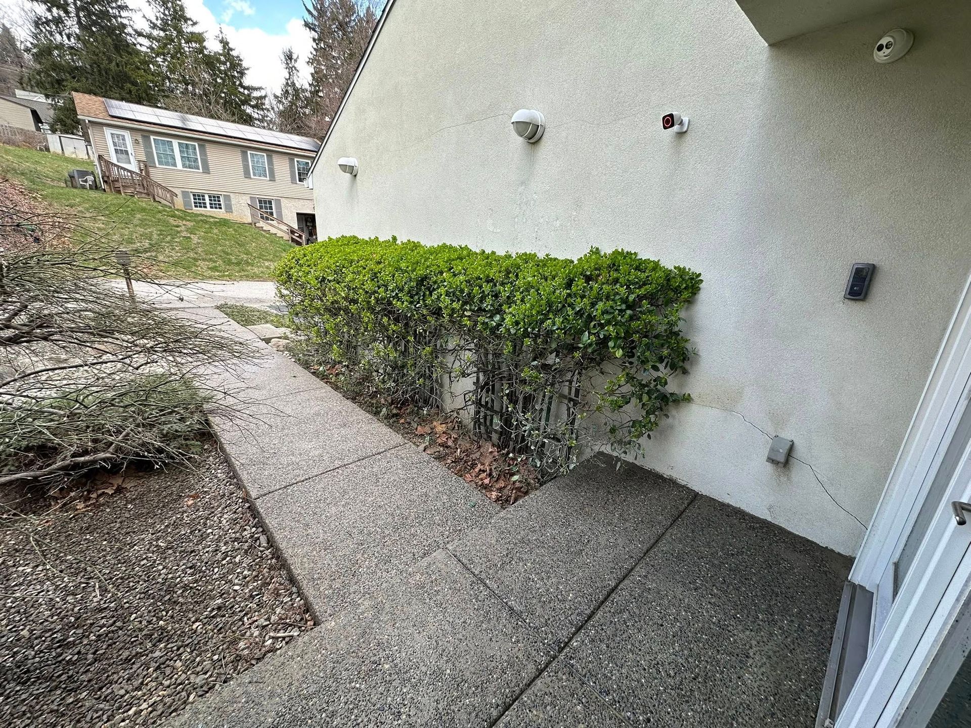 Apartment walkway with concrete path, trimmed hedge, and beige building wall