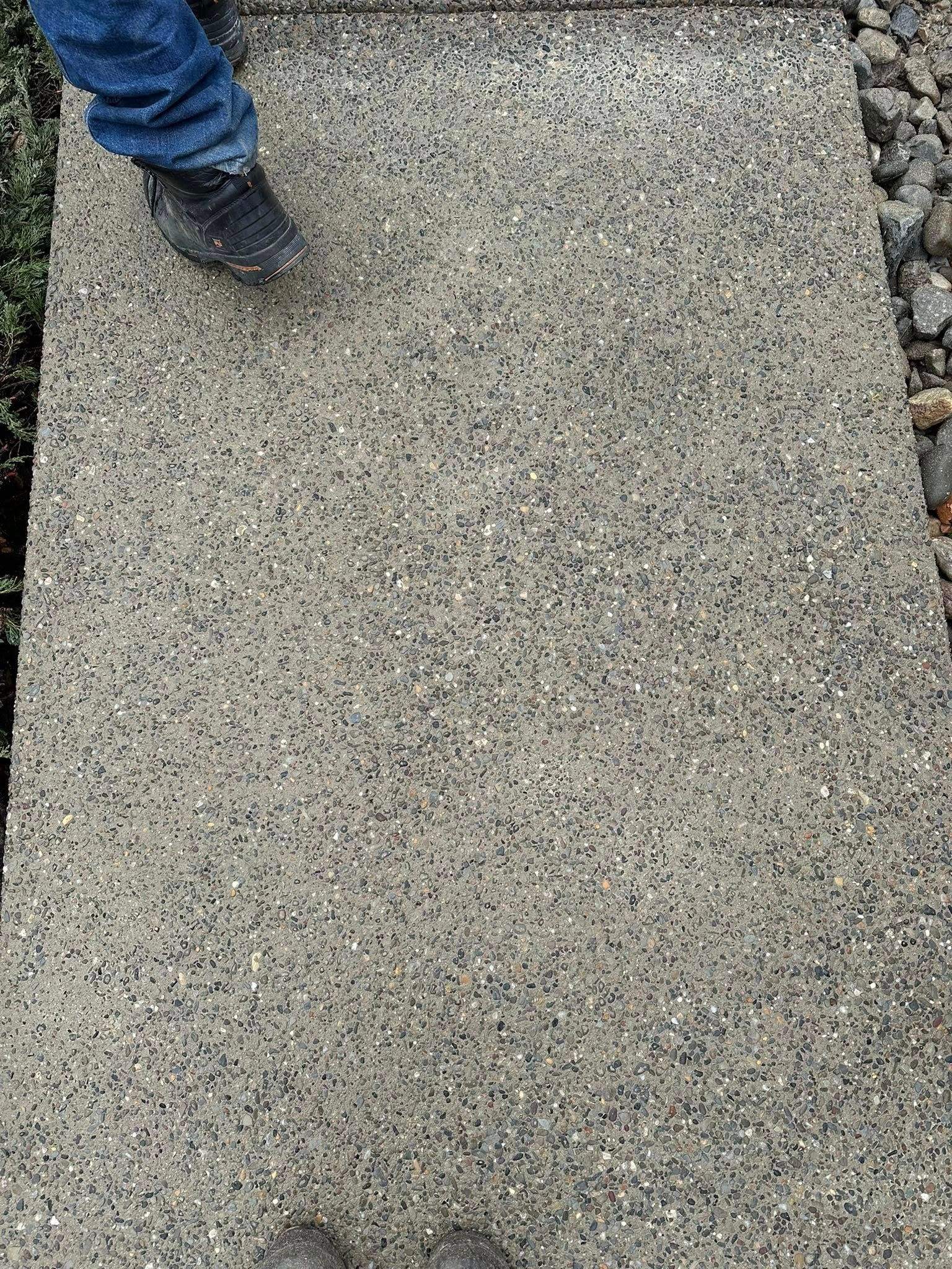 Person in jeans and a black boot standing on a gravel path.