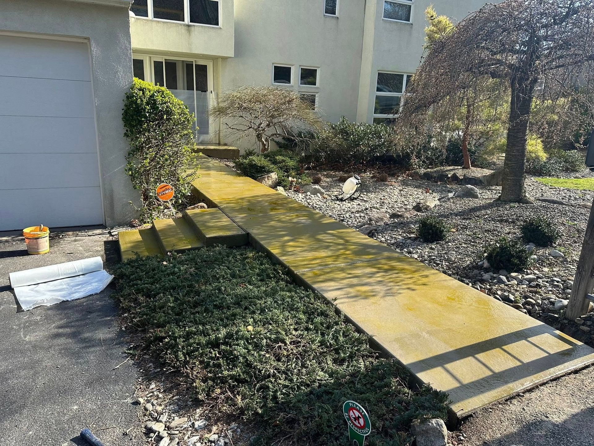 Residential walkway with a yellow wooden ramp leading to a house entrance, bordered by bushes and a garage door