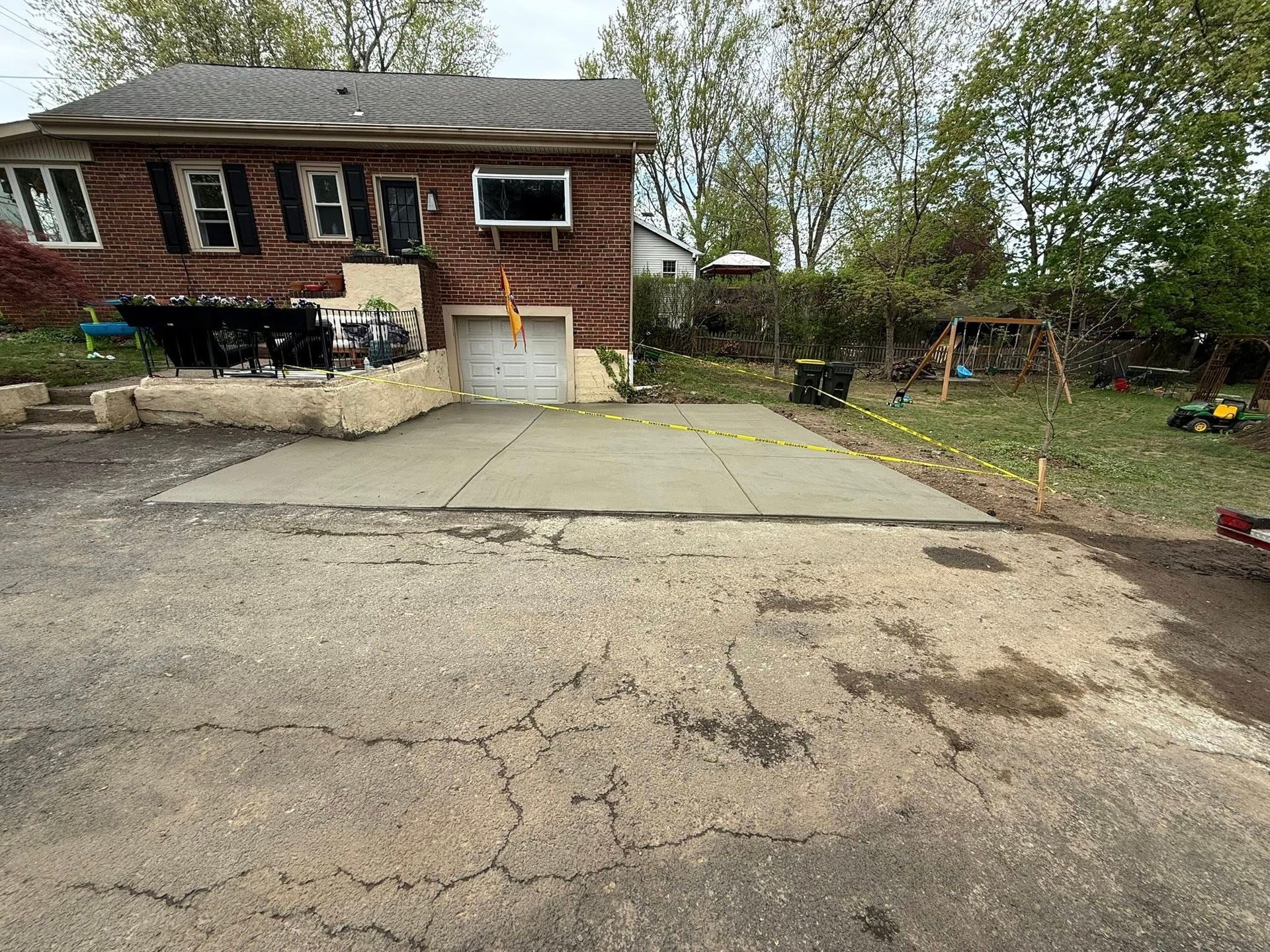 Brick house with cracked concrete driveway and a small yard with trees and a fence
