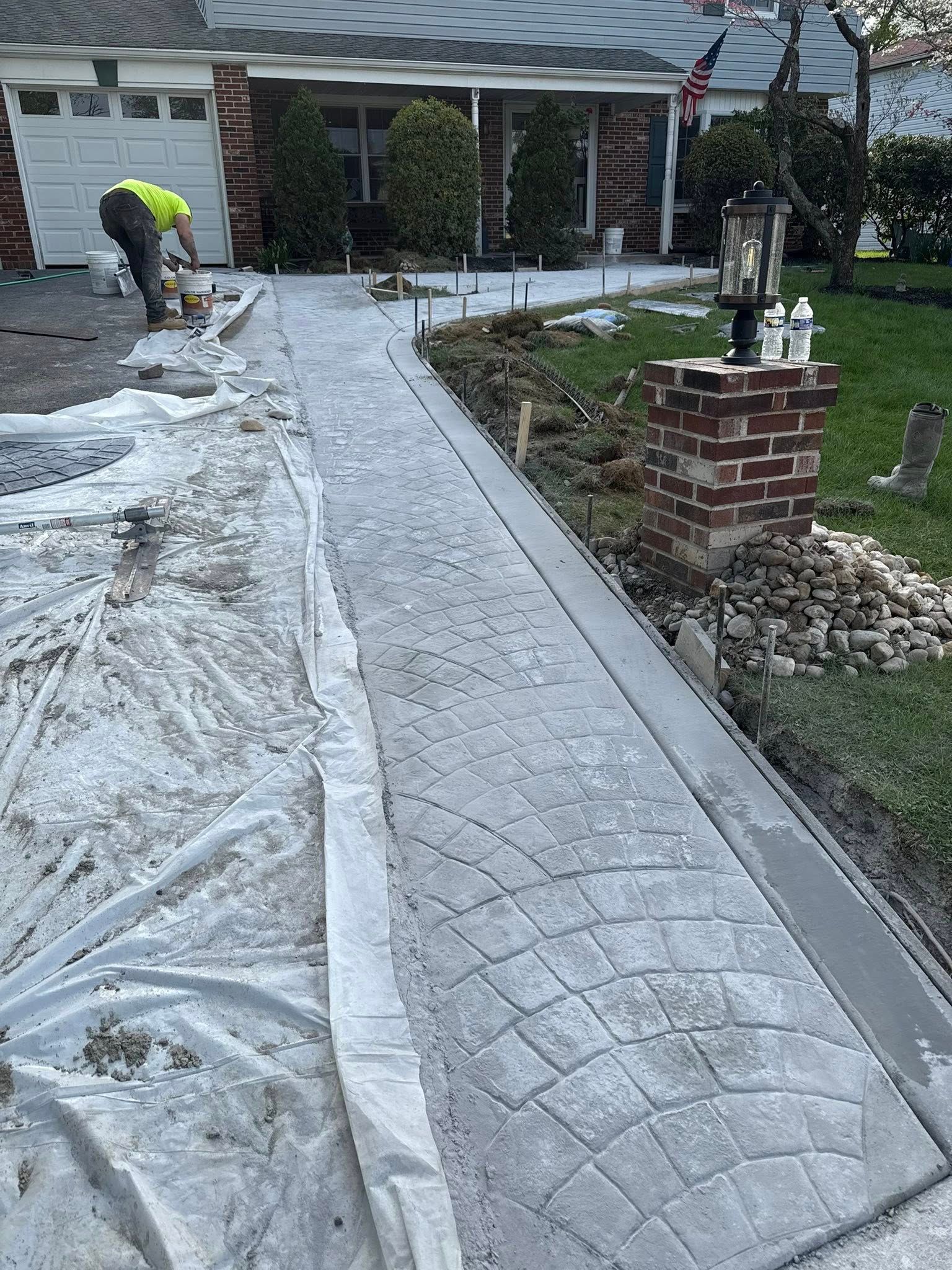 Worker installing gray paver walkway beside a house, with edging and landscaping underway