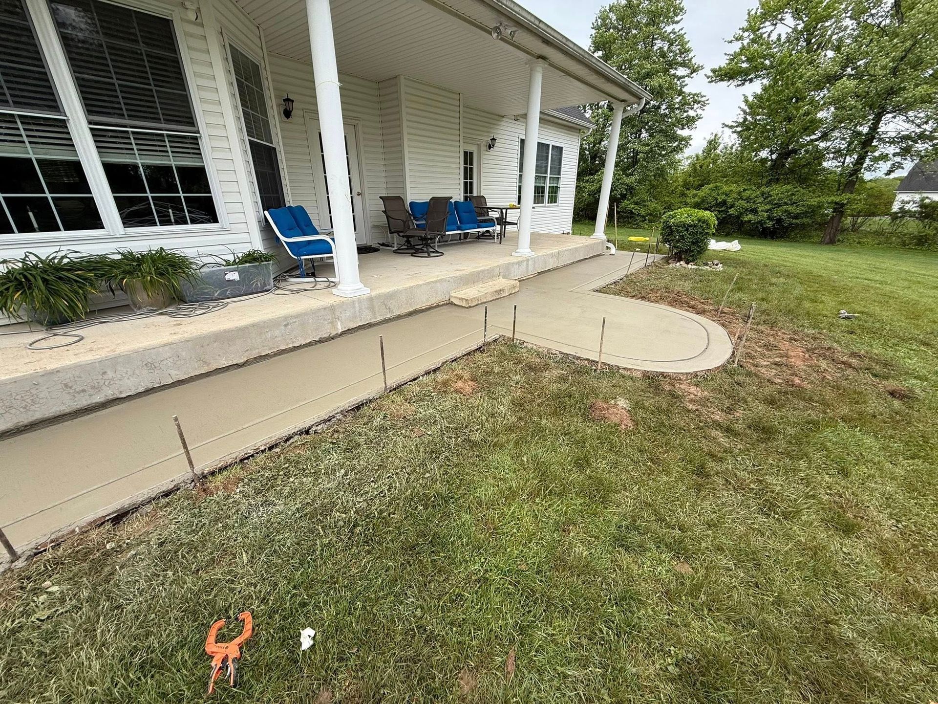 House porch with blue chairs and a concrete walkway beside a grassy yard
