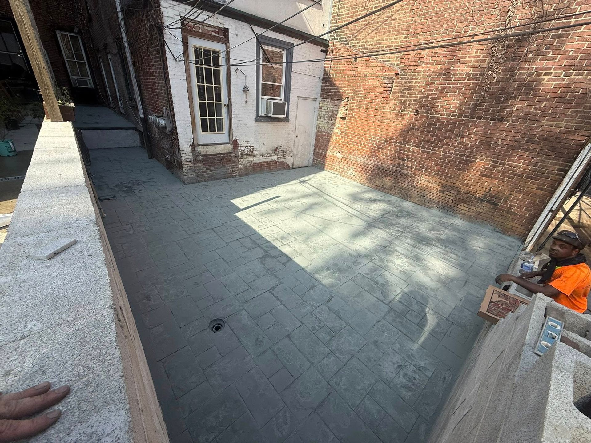 Empty brick-paved courtyard beside a white shed and red brick wall, with a handrail in the foreground.