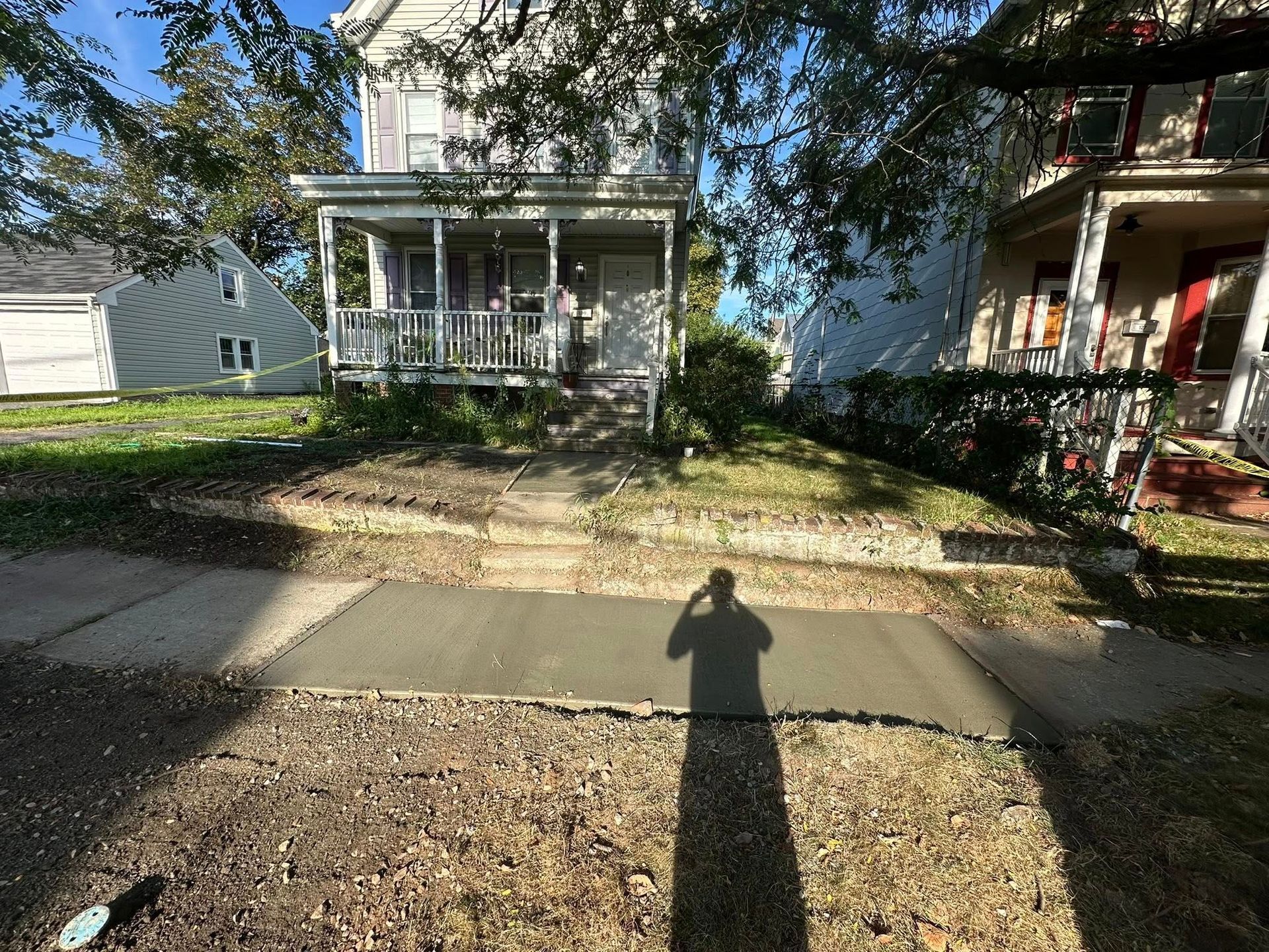 Residential street with two small houses, a sidewalk, and long afternoon shadows cast across the yard.