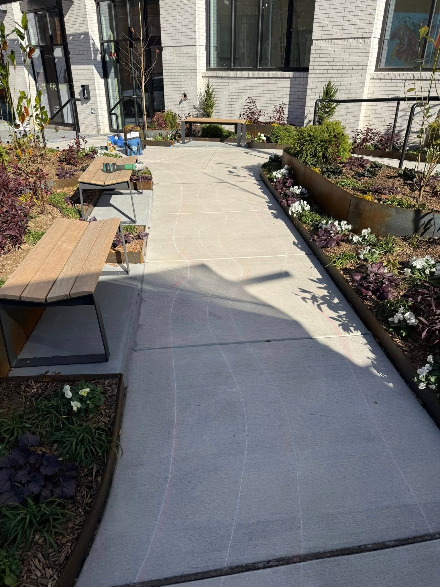Concrete walkway through a small garden patio with benches, raised planters, and a house entrance ahead.
