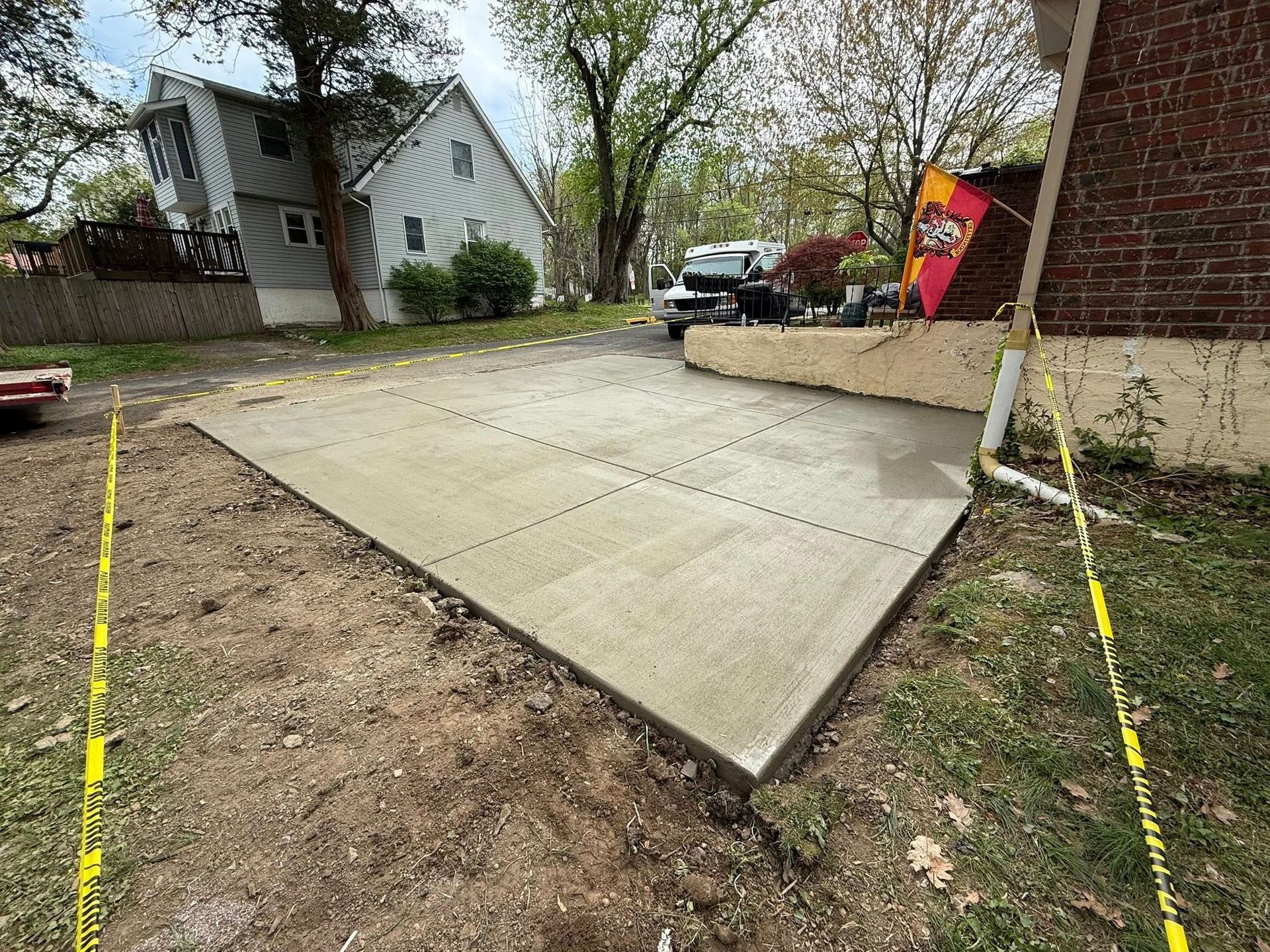 New concrete driveway and walkway beside a house, marked by yellow survey stakes.
