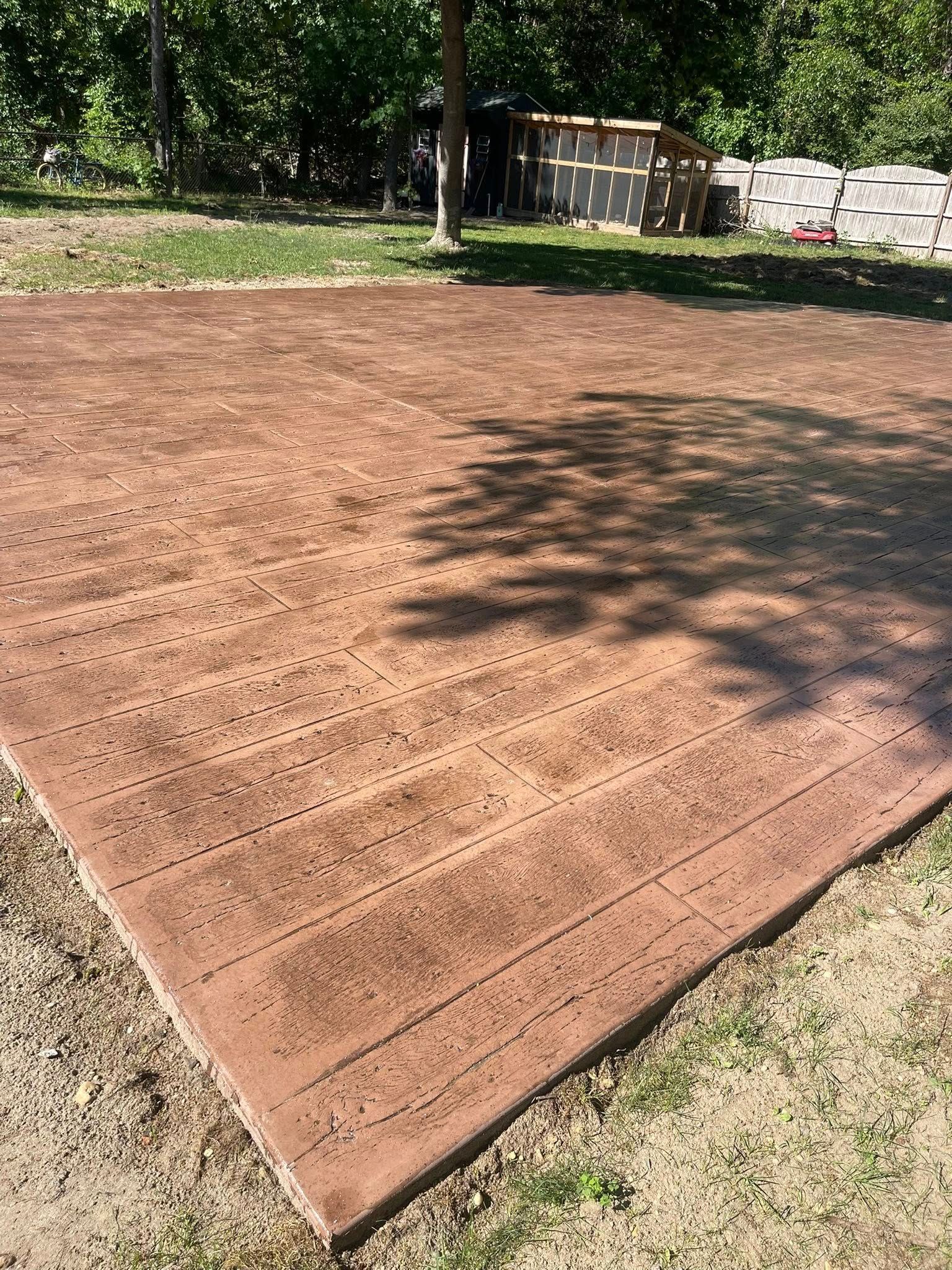 Freshly leveled reddish-brown gravel pad in a yard, with trees and a shed in the background.