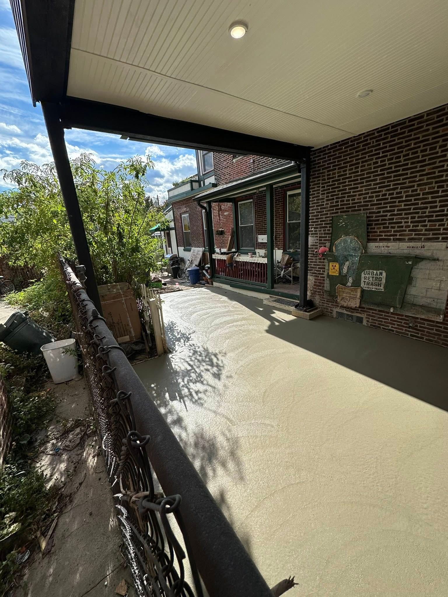 Covered sidewalk outside a storefront, with brick walls, hanging plants, and bright sunlight ahead