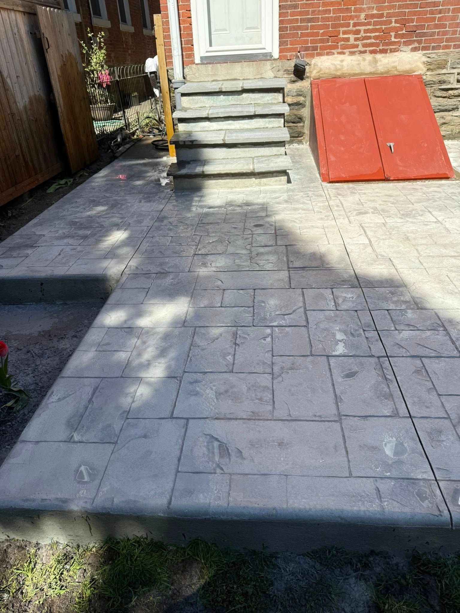 Front walkway with stone pavers leading to a short step, beside a red ramp and wooden fence.