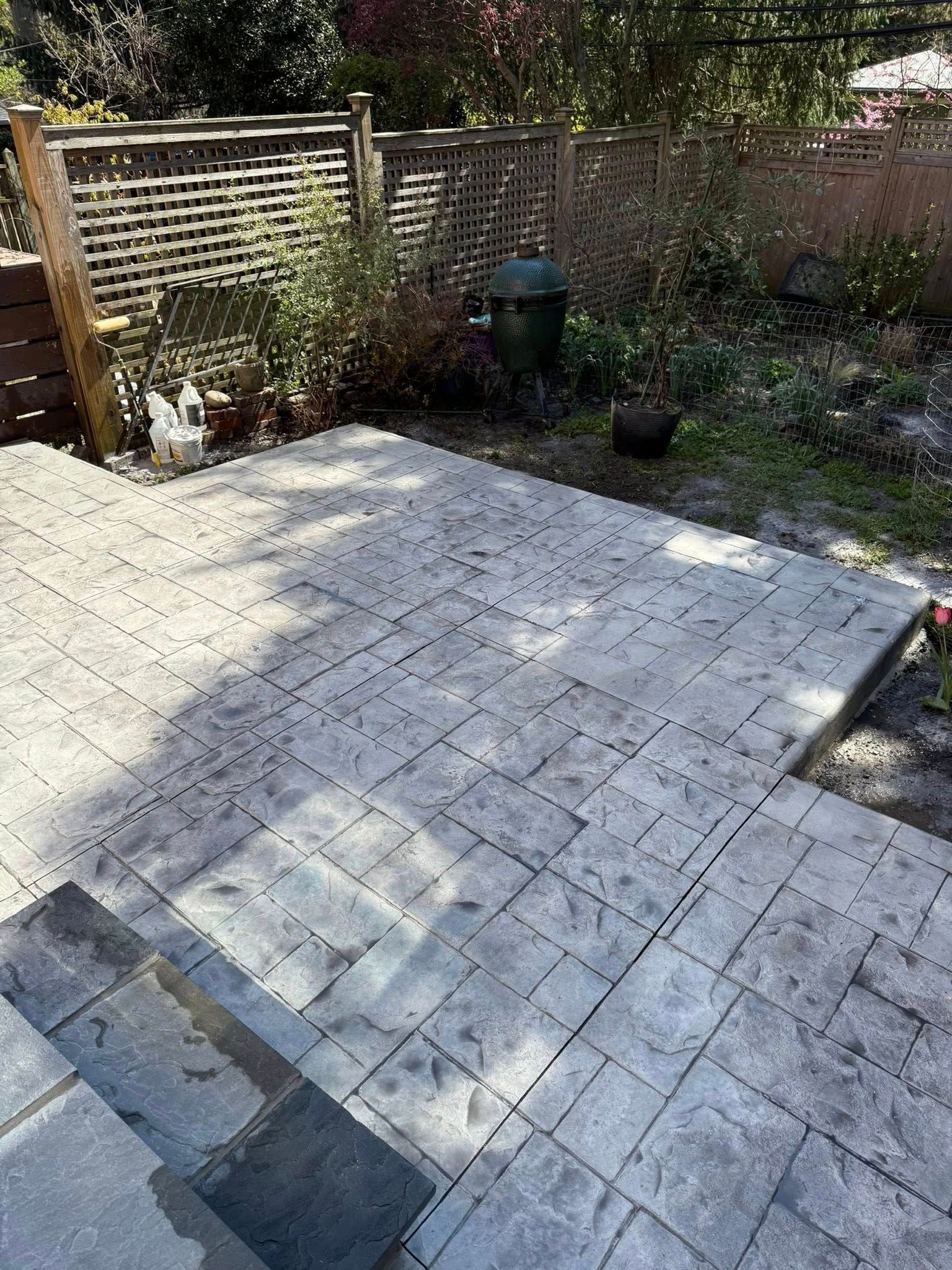 Sunlit stone patio in a backyard garden with a brick wall, fence, and potted plants
