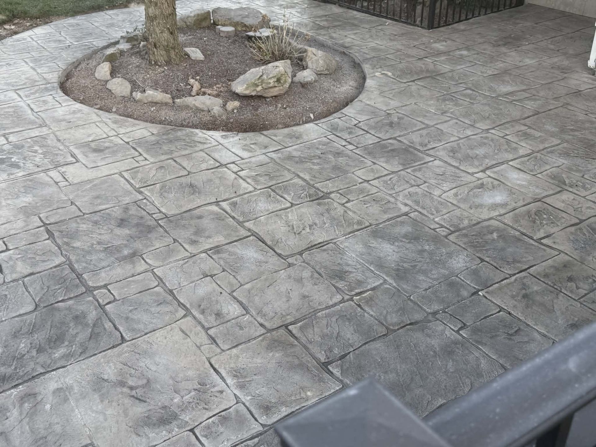 Paved stone courtyard with a tree in a circular gravel bed and a bench edge in the foreground