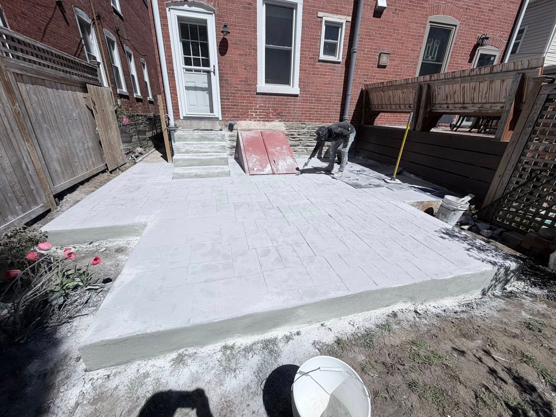 Backyard with a large concrete patio, brick house steps, wooden fences, and a basketball on the grass