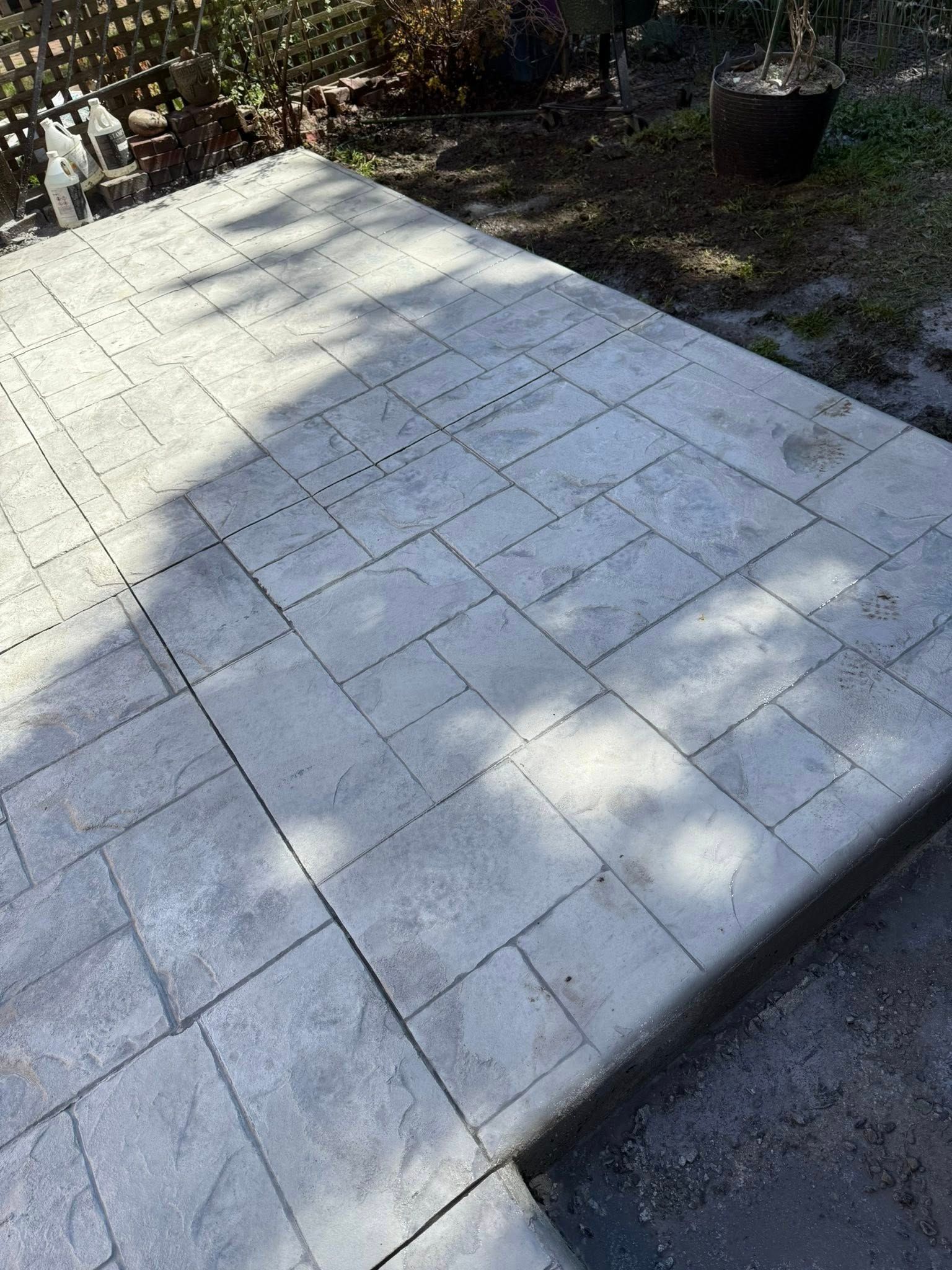 Paved stone patio with a stepped edge, dappled sunlight, and a small garden border nearby