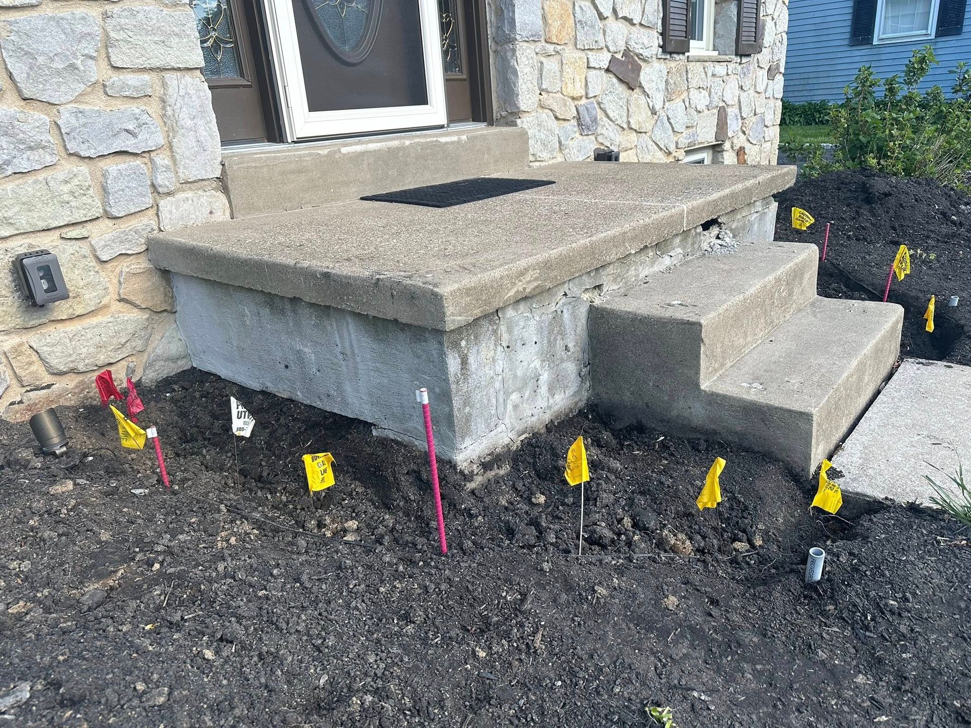 Stone front steps beside a house, with fresh soil and small colored flags marking the landscaping below.
