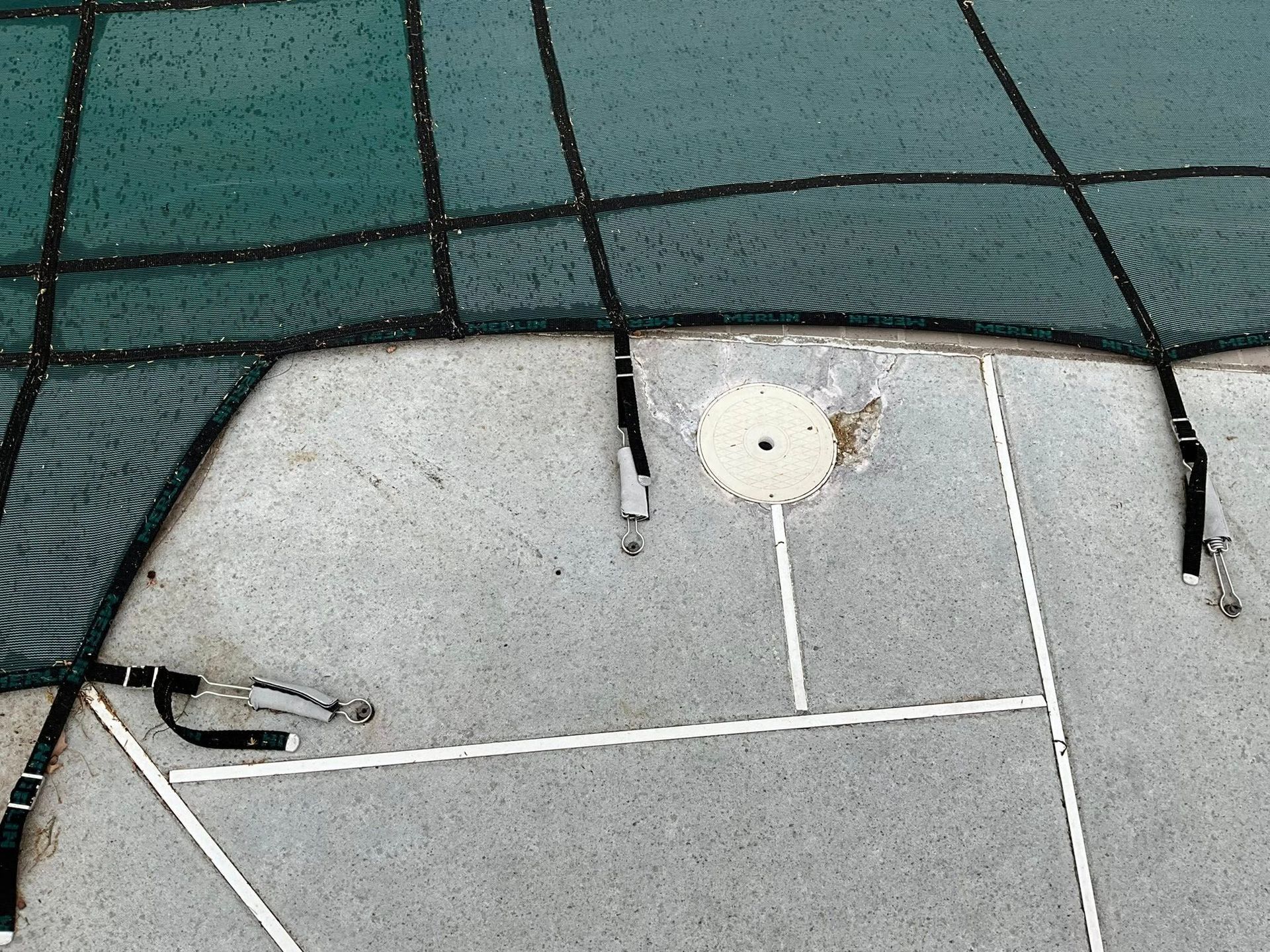 Hole in a green net over a gray tennis court surface with white lines