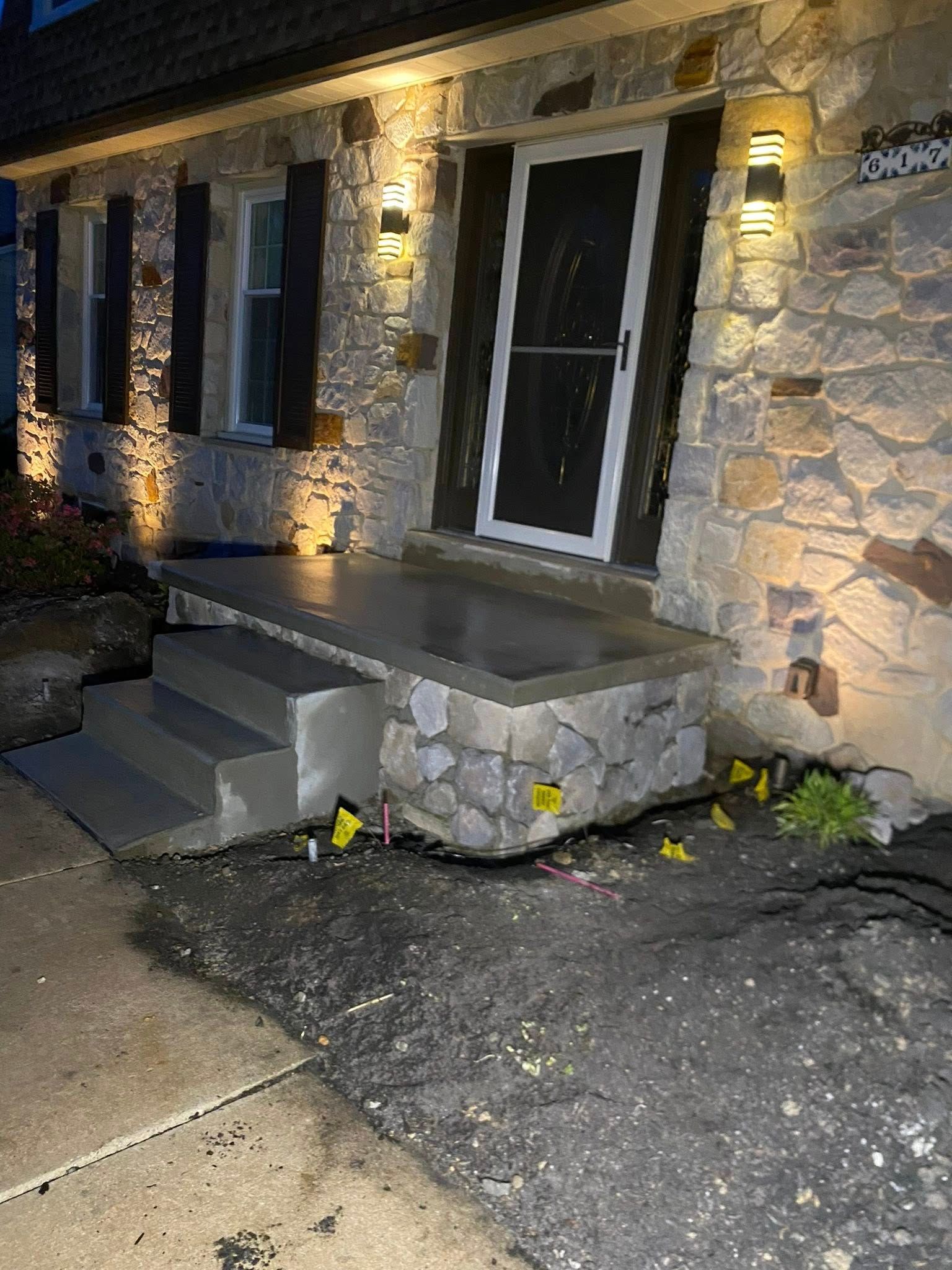 Stone house entryway with lit wall sconces, concrete steps, and a glass front door at night