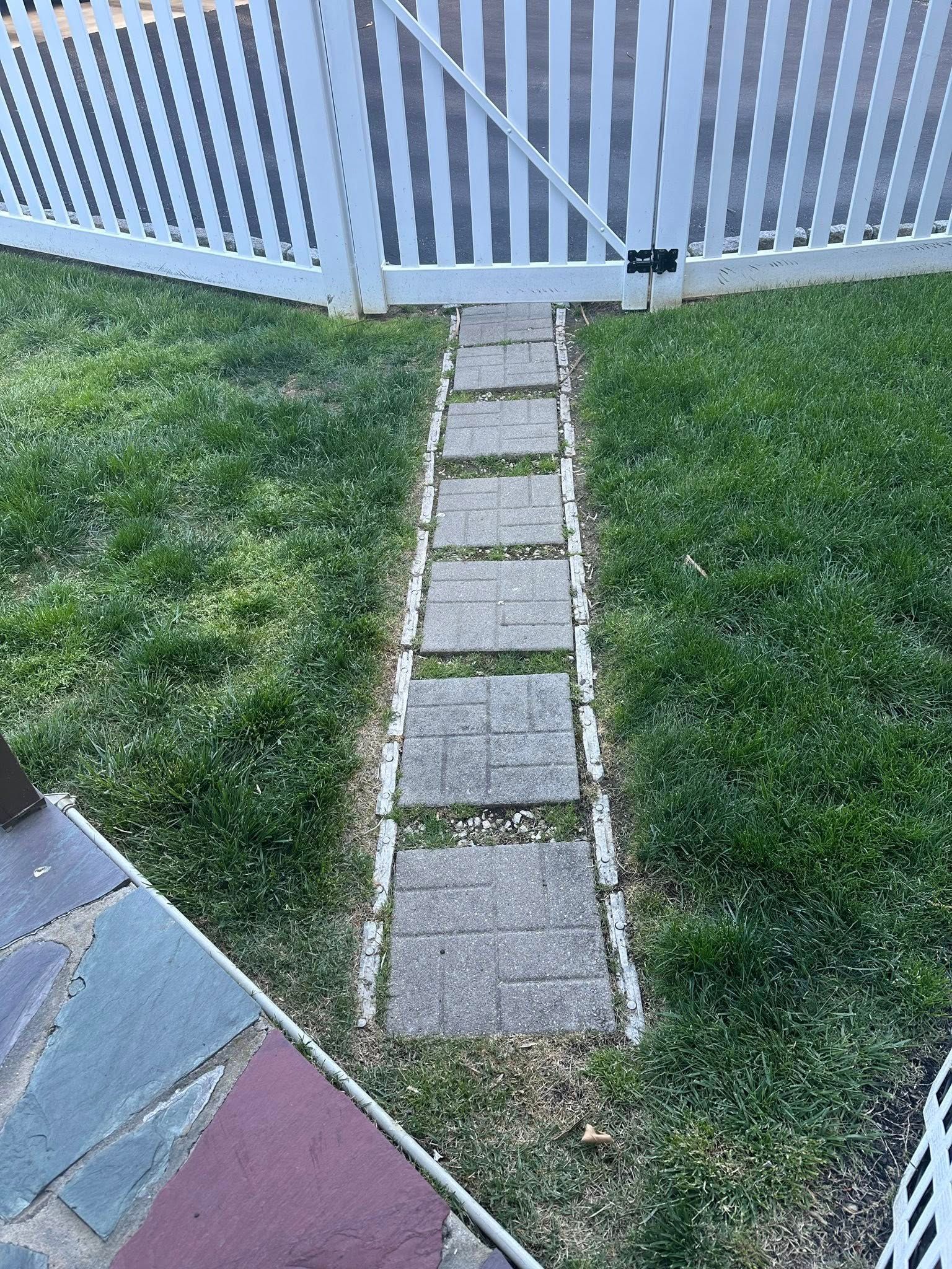 Narrow stone path leading to a white gate across a grassy yard