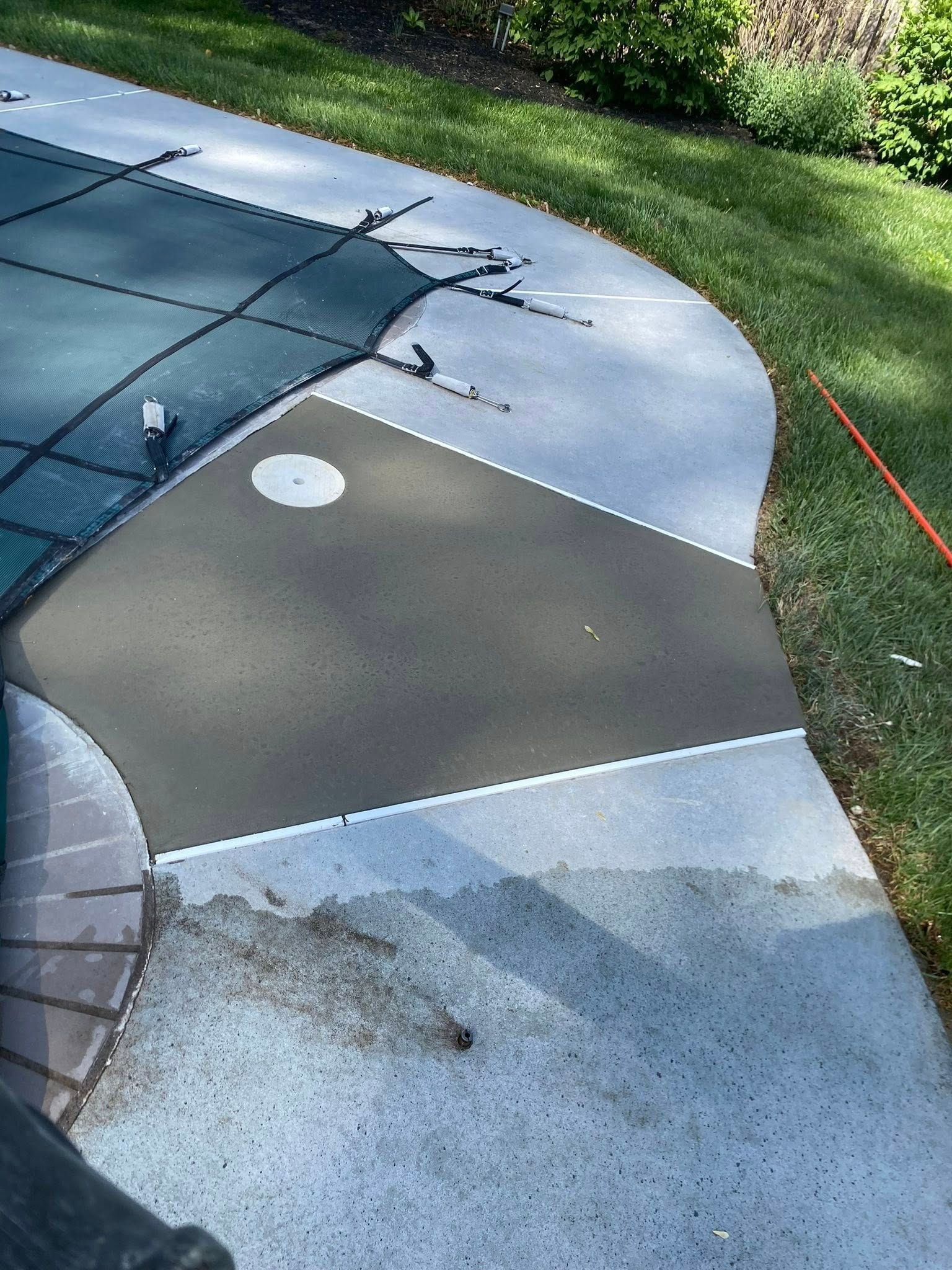 Backyard concrete patio with a dark tarp-covered section and grassy lawn along the edge