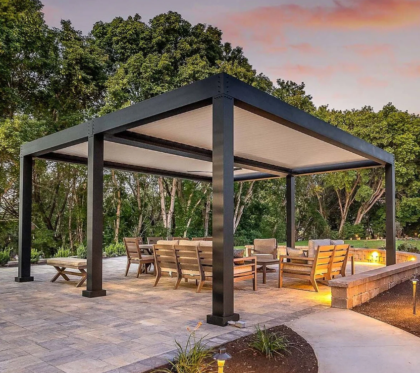 Modern outdoor pavilion with seating on a stone patio, surrounded by trees at sunset