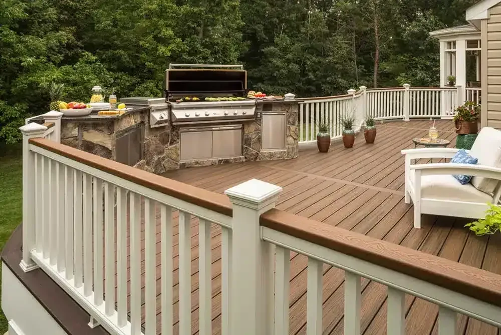 Wooden deck patio with built-in grill, white railing, outdoor seating, and trees in the background