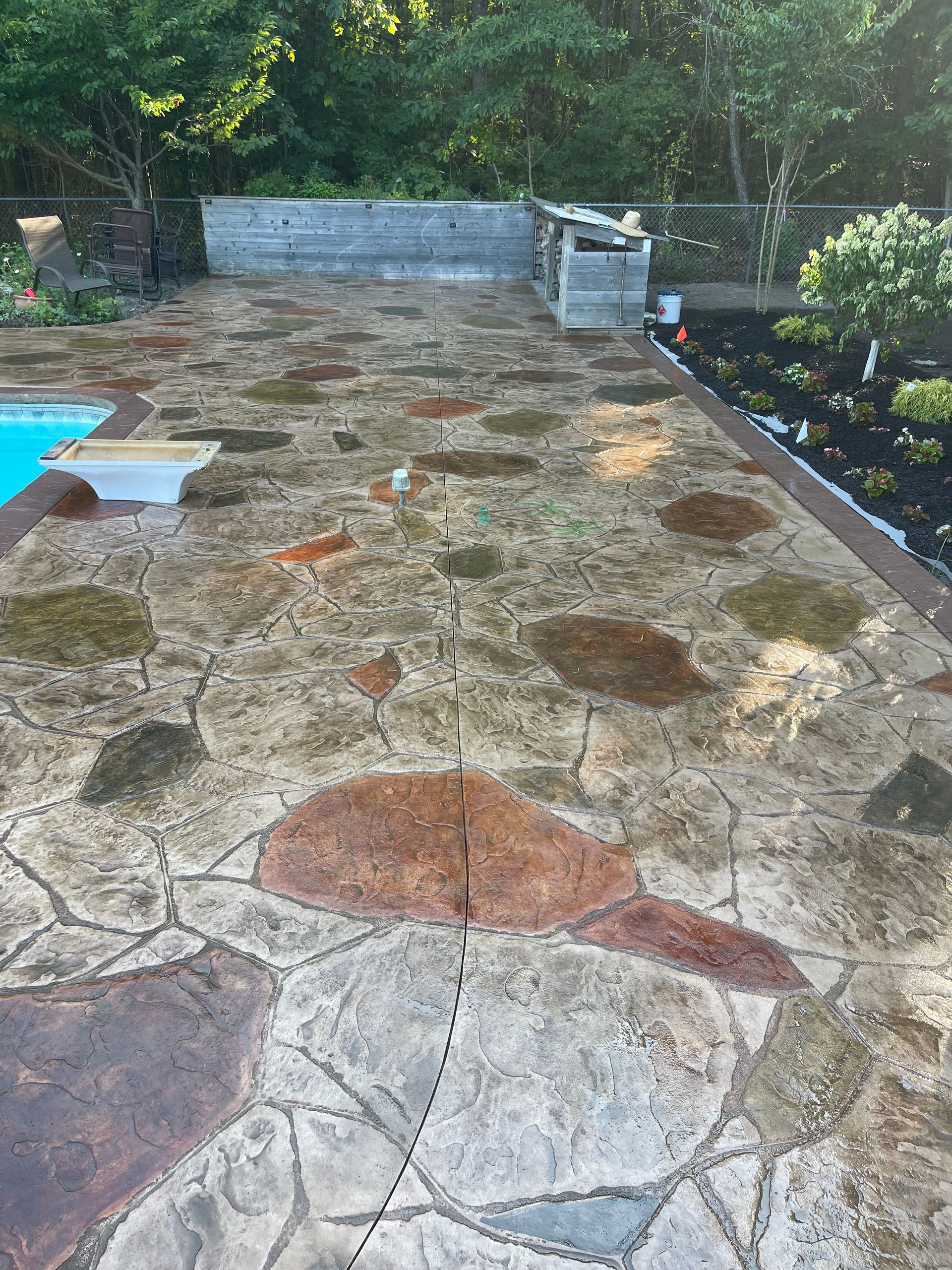 Stone patio with irregular paving, a pool edge on the left, and greenery along the back and right sides.