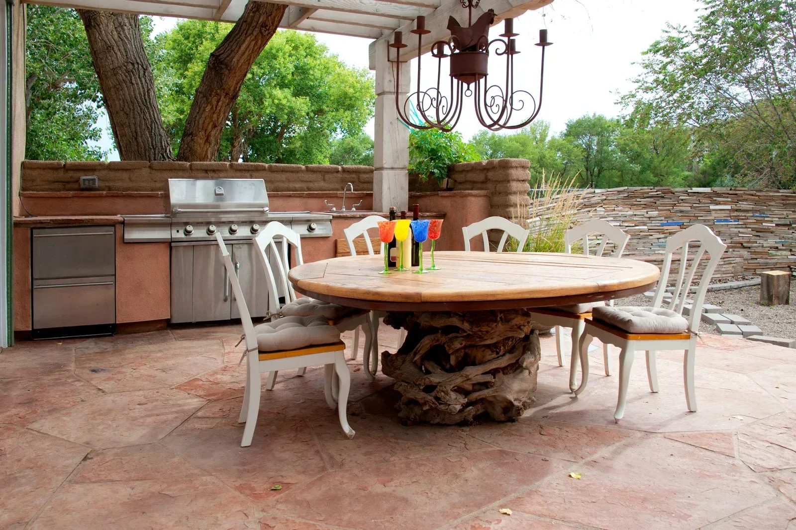 Outdoor patio with round stone table, white chairs, and a built-in grill under a covered pergola.