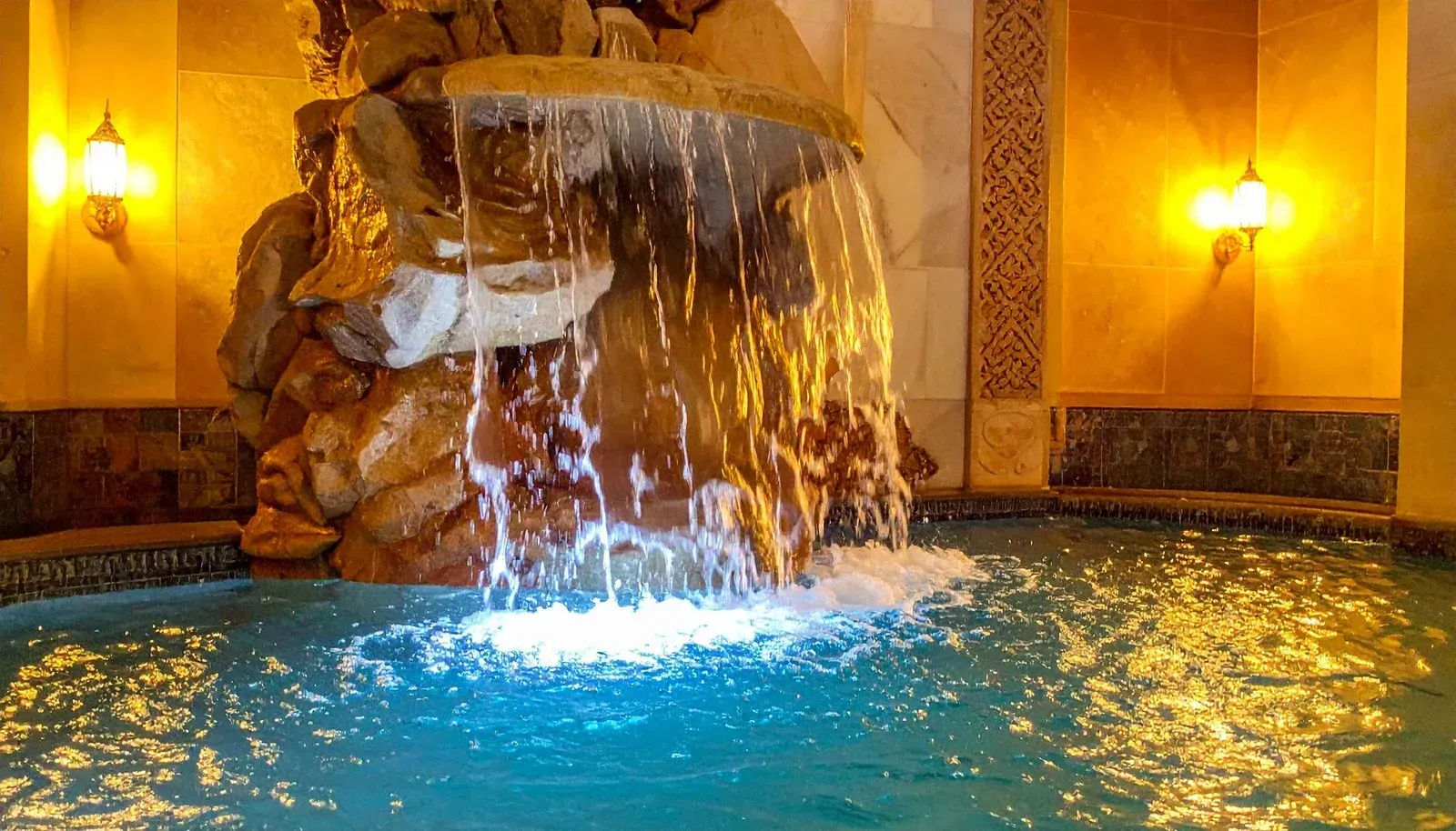 Indoor fountain spilling into a turquoise pool under warm yellow lights