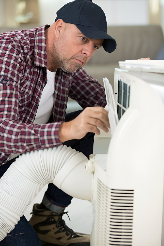 A Man Is Fixing An Air Conditioner With A Hose Attached To It — Mason's Air Conditioning Pty Ltd in Pittsworth, QLD