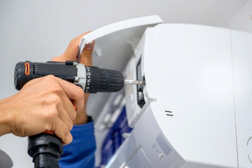 A Person Is Using A Drill To Fix An Air Conditioner — Mason's Air Conditioning Pty Ltd in Drayton, QLD