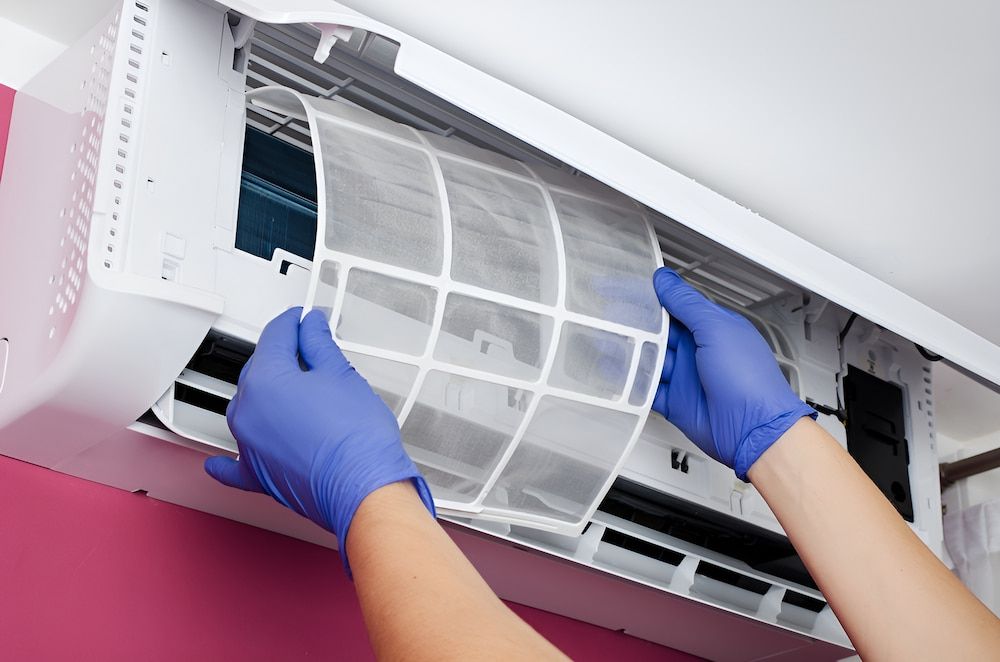 A Person Wearing Blue Gloves Is Cleaning An Air Conditioner — Mason's Air Conditioning Pty Ltd in Gatton, QLD